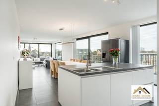 Vanuit dit prachtige penthouse bent u vanaf dag 1 ook de eigenaar van de volledige skyline van Wachtebeke-centrum. De bijzonder lichtrijke leefruimte met open keuken baadt in het daglicht door de grote raampartijen en zo ziet u vanuit elke hoek het dagelijkse leven in het dorp als een continue bewegend schilderij voorbij glijden - zonder er evenwel enige last van te ondervinden. De keuken is voorzien van alle moderne comfort, vanachter het ruime kookeiland is er eveneens altijd een bijzonder uitzicht. Net naast de keuken is er een grote opslagruimte/wasplaats aanwezig. Een lange gang (rechtstreeks bereikbaar met de lift en uiteraard ook via de trap) brengt je tot in de twee slaapkamers, waarvan de grootste is voorzien van een mooie dressing. De badkamer beschikt over een riante inloopdouche, en in de gang is er een apart toilet aanwezig. Van het buitenleven genieten doe je op het grote zonovergoten terras, dat via de schuifdeuren van de leefruimte bereikbaar is. Er is verplicht een garage aan te kopen voor €25 000 en een parkeerplaats in het gebouw inbegrepen de prijs. Nog 3 jaar vrijgesteld van OV. Inschrijvingen via mail naar tommy@immo-home.be, geen telefonische inschrijvingen! Volg ons op Fb en insta. Voor meer info: www.immo-home.be GRATIS SCHATTING GRATIS FINANCIEEL ADVIES