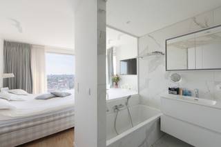 <p><strong>Exclusief penthouse-appartement met panoramisch stadszicht</strong></p>
<p>Op een van de hoogste verdiepingen van deze moderne moderne Antwerp Tower ligt dit sfeervolle en luxueus afgewerkte appartement, met een adembenemend uitzicht over de stad dat je doorheen de hele woning blijft begeleiden. Vloerhoge ramen laten overal het licht binnenstromen en brengen de skyline, de torenspitsen en de haven tot in de leefruimtes.</p>
<p>De inkomhal leidt naar een ruime living waar een opvallende betonnen kolom een architecturaal accent vormt tussen de zithoek en leefruimte. Warme houten vloeren en een verzorgde, hedendaagse afwerking geven de ruimte een tijdloze uitstraling. De living loopt over in de volledig geïnstalleerde open keuken, met kookeiland, zitbar, ingebouwde wijnkoeler en een marmeren achterwand — een plek waar koken en samenzijn moeiteloos in elkaar overvloeien.</p>
<p>De hoofdslaapkamer vormt een rustige plek met zicht over de stad. Een glazen wand verbindt de kamer visueel met de ensuite badkamer, volledig afgewerkt in marmer, met ligbad, enkele wastafel op een zwevend meubel en een inloopdouche. Een tweede badkamer met inloopdouche en dubbele wastafel bedient de andere slaapkamer, die nu gebruikt wordt als studie, aangevuld met een apart gastentoilet voor extra comfort.</p>
<p>Het buitenterras fungeert als een natuurlijk verlengstuk van de leefruimte — de ideale plek om te genieten van het uitzicht, van ochtendkoffie tot zonsondergang.<br />Uw wooncomfort wordt verhoogd met een parkeerplaats in de ondergrondse parkeergarage voor 60.000 EUR.</p>
<p>Een appartement waar licht, ruimte en uitzicht samenkomen tot één vloeiend geheel.</p>