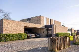 Deze moderne villa uit 2016 is gelegen op een uitzonderlijk breed perceel van ruim een halve hectare (5.016 m²) en combineert hedendaags comfort met een rustige, groene omgeving. Het ontwerp kenmerkt zich door een tijdloze architectuur, waarbij de indrukwekkende raampartijen zorgen voor een uitzonderlijke lichtinval en een naadloze overgang tussen binnen en buiten.<br /><br />De woning is ook praktisch ingericht voor wie wonen en werken wil combineren. Er zijn twee ruimtes voorzien die geschikt zijn voor een professionele activiteit aan huis. <br /><br />In de leefruimte staat ruimtelijkheid en wooncomfort centraal.<br /><br />De keuken is volledig uitgerust met premium toestellen van Gaggenau en een Quooker-kraan. Van hieruit, alsook de gehele leefruimte, geniet u van een weids vergezicht over de zuidoost georiënteerde tuin en de achterliggende natuur. <br /><br />Achter de keuken bevindt zich praktisch een grote berging, die ook toegankelijk is via de carport. Over de gehele woning zijn voldoende maatkasten voorzien, een tweede grote berging en een aparte wasruimte die ook van een douche is voorzien.<br /><br />De woonbeleving wordt verder naar een hoger niveau getild door een slim domoticasysteem, camerabewaking, alarmsysteem en een geïntegreerde muziekinstallatie die doorheen de woning voor de juiste sfeer zorgen.<br /><br />In totaal zijn er vijf slaapkamers en twee badkamers. De master bedroom beschikt over een ensuite badkamer en dressing met zicht op het groen, wat zorgt voor een rustige en aangename sfeer.<br /><br />Met een energielabel A en conforme elektriciteit is ook aan duurzaamheid en technische kwaliteit gedacht, wat het geheel toekomstgericht maakt. Deze lichtrijke villa vormt zo een perfecte balans tussen moderne architectuur, comfort en een unieke ligging in het groen.