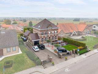 In het centrum van Nieuwkerke bevindt zich deze bijzondere voormalige directeurswoning uit 1923. Een karaktervolle eigendom waarin authentieke elementen, royale ruimtes en hedendaags comfort op een mooie manier samenkomen. De statige gevel, hoge plafonds en bewaarde originele details geven het pand een unieke uitstraling. Dankzij de centrale ligging en de veelzijdige indeling leent deze eigendom zich uitstekend voor verschillende doeleinden. Naast een ruime gezinswoning behoort ook een combinatie van wonen en werken, een B&amp;B-concept of een horecazaak met woongelegenheden tot de mogelijkheden.<br /><br />Bij binnenkomst zorgt de inkomhal meteen voor een aangename eerste indruk. Op het gelijkvloers bevindt zich momenteel een sfeervol restaurantgedeelte met plaats voor 34 gasten. Aan de voorzijde sluit het zonnige terras hier mooi op aan, met ruimte voor ongeveer 40 personen. De volledig uitgeruste bar en professionele keuken vormen samen een praktische en sfeervolle horecaruimte. Vanuit de bar is er bovendien toegang tot een ruime kelder, ideaal als extra opslagruimte.<br /><br />De eerste verdieping omvat een comfortabel appartement met een bijzonder lichtrijke leefruimte en mooi uitzicht over de tuin en de omgeving van Nieuwkerke. Daarnaast beschikt deze verdieping over een bureauruimte, een ruime slaapkamer met rechtstreekse toegang tot de badkamer en een afzonderlijke, volledig ingerichte keuken. De badkamer is uitgerust met een dubbele lavabo, inloopdouche en toilet.<br /><br />Ook de tweede verdieping werd ingericht als volwaardig appartement. Hier zorgen de open indeling en de vele lichtinval voor een aangename woonbeleving. De leefruimte sluit rechtstreeks aan op de keuken en de ruime slaapkamer beschikt over een open badkamer, wat zorgt voor een eigentijdse loftsfeer. Een bijkomende badkamer met dubbele lavabo, toilet en inloopdouche biedt het nodige comfort.<br /><br />Achteraan bevindt zich een verrassend ruime en groene tuin, een rustige plek midden in het centrum. Het voorste gedeelte doet momenteel dienst als terras voor het restaurant. Verder zijn er twee ruime bergingen aanwezig, waarvan één voorzien is van een pizzaoven. Deze ruimtes bieden tal van mogelijkheden voor opslag, hobby's of een creatieve invulling. Daarnaast beschikt de tuin over een verzorgde moestuin en kippenren. Een bijkomende troef is de achteruitgang naar de Steenwerkstraat, samen met parkeermogelijkheid naast het pand. Zo combineert de eigendom een centrale ligging met een uitzonderlijk ruime buitenomgeving.<br /><br />In 2017 werd het pand grondig gerenoveerd, waarbij veel aandacht werd besteed aan het behoud van het authentieke karakter én het hedendaagse comfort. Zo werden onder meer de leidingen vernieuwd, het dak aangepakt en een ventilatiesysteem en zonnepanelen geplaatst. Ook werden waterverzachter en brandwerende plafonds en deuren voorzien.<br /><br />Een eigendom met geschiedenis, uitstraling en bijzonder veel mogelijkheden. Of u nu op zoek bent naar een ruime woning, een karaktervol horecapand, een B&amp;B-concept of een combinatie van wonen en werken: deze voormalige directeurswoning biedt een unieke basis in het hart van Nieuwkerke. Interesse in dit veelzijdige pand? Contacteer ons vandaag nog voor meer informatie of een bezoek ter plaatse.