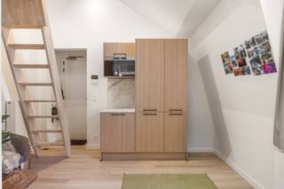 Op een uitzonderlijke ligging in het historische centrum van Leuven, in een zijstraat van de Naamsestraat en van de Oude Markt, bevindt zich deze kwalitatief afgewerkte duplex studentenkamer in Residentie Estelle. De kamer is gelegen op de derde verdieping aan de achterzijde van het gebouw en heeft een oppervlakte van ca. 15 m². De duplexindeling met mezzanine zorgt voor een aangename scheiding tussen de leef- en slaapruimte. Ze beschikt over een eigen badkamer met douche, lavabo en toilet en is daarnaast voorzien van een op maat gemaakte kledingkast en een praktisch ontbijtblok met koelkast en microgolfoven. De bewoners kunnen tevens gebruikmaken van een stijlvolle en volledig uitgeruste gemeenschappelijke keuken met onder meer een vaatwasser, diepvriezer en inductiekookplaat. Residentie Estelle combineert een karaktervolle, beschermde gevel met hedendaags wooncomfort en beschikt onder meer over ventilatiesysteem D met warmteterugwinning. De ligging vormt een absolute troef, midden in het Leuvense studenten- en stadscentrum, met verschillende KU Leuven-faculteiten, winkels, horeca en openbaar vervoer op wandelafstand. De kamer wordt momenteel verhuurd aan een netto huurprijs van €683,4 per maand en vormt daarmee een interessante investering in het centrum van Leuven. De verkoopprijs bedraagt €219.000. De verkoop valt onder het stelsel van de registratierechten.