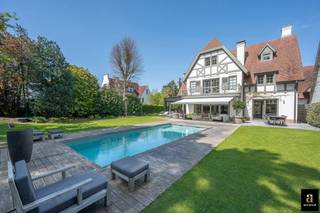 Prachtige, imposante villa rustig gelegen in een charmant paadje in hartje Zoute, op wandelafstand van de winkels, de zee en het strand. Indeling: inkomhal met vestiaire en gastentoilet. Ruime woonkamer met haard, tv-hoek met bureauruimte en eetplaats. Heel lichtrijke benedenverdieping dankzij de grote raampartijen die uitgeven op de perfect aangelegde tuin met zwembad. Aangename leefkeuken met ontbijthoek. Op de eerste verdieping: ruime master bedroom met toegang tot het terras, dressing en ensuite badkamer (dubbele lavabo, ligbad, inloopdouche en apart toilet). Bureau/ tweede slaapkamer. 3de slaapkamer met douchekamer, keuken en woonkamer (kan dienen als studio/concierge). Op de tweede verdieping bevinden zich 2 ruime slaapkamers. Badkamer. De villa is onderkelderd en bestaat uit vergaderzaal/ontspanningsruimte, wasplaats en technische ruimte. Prachtig aangelegde tuin met terras en verwarmd zwembad. Inpandige garage voor twee wagens en outdoor parking voor meerdere wagens. De villa geniet van een perfecte oriëntatie, werd afgewerkt met oog voor detail. De villa werd eveneens voorzien van een airco-systeem, automatische besproeiing, alarm.