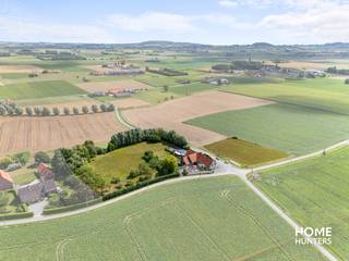 Te midden van de uitgestrekte velden bevindt zich deze uitzonderlijke eigendom waar rust en luxe samenkomen op een perceel van 11.187m². Dit historisch landgoed werd met oog voor detail gerenoveerd tot een instapklare parel, waar de combinatie van authentiek karakter en moderne architectuur zorgt voor een unieke woon- en belevingservaring. Dankzij de succesvolle B&B, de aanpalende herberg en de luxueuze privéwoning biedt dit domein bovendien een interessante opportuniteit voor wie op zoek is naar een levensproject met rendement. Het eigendom wordt beschouwt als "Handelshuis"<br /><br />De hoofdwoning charmeert met hoge plafonds, overvloedige glaspartijen en een lichtrijke leefruimte met zicht op de uitgestrekte tuin. De leefruimte sluit naadloos aan op een volledig uitgeruste keuken met keukeneiland. Een mezzanine met zicht op de tuin fungeert als bureau of hobbyruimte. De woning telt zes slaapkamers, waarvan vijf momenteel worden uitgebaat als volwaardige B&B-kamers met elk een eigen badkamer en toiletvoorziening. De master bedroom beschikt over een aparte dressing en een privé badkamer.<br /><br />Daarnaast is er een volledig uitgeruste wellnessruimte met hammam, infraroodsauna en jacuzzi en een ruim zonneterras dat grenst aan de perfect onderhouden tuin. De aanpalende herberg straalt authenticiteit uit en leent zich uitstekend voor evenementen of een horecazaak in combinatie met het gastenverblijf. <br /><br />Op technisch vlak is het geheel tot in de puntjes afgewerkt: vloerverwarming is per kamer regelbaar, het energieverbruik is optimaal dankzij een EPC-label A, 83 zonnepanelen, ongeveer 40 kW aan batterijopslag en een geothermische warmtepomp. Een ruime garage van 98 m² en zes extra parkeerplaatsen maken het eigendom compleet.<br /><br />Een uitzonderlijke eigendom die moeiteloos wonen en visie op de toekomst combineert — en dat alles in een groene omgeving.<br /><br />Contacteer ons nu voor een plaatsbezoek en ontdek zelf de charme van dit exclusieve eigendom!