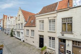 Op een bijzonder charmante locatie in de Brugse binnenstad, op een steenworp van het Astridpark en de Vismarkt, ontdekken we deze sfeervolle stadswoning met een verrassende indeling over verschillende niveaus. Achter de authentieke gevel schuilt een gezellige woning waar karaktervolle elementen en hedendaags wooncomfort harmonieus samengaan. De houten balkenplafonds, warme materialen, charmante trapjes en speelse niveauverschillen zorgen voor een unieke woonbeleving.<br /><br />Op het gelijkvloers bevindt zich een gezellige eet- en leefruimte met aansluitend een ingerichte keuken, uitgevoerd in een stijlvol contrast van donkere keukenkasten en lichte accenten. Verder beschikt deze verdieping over een badkamer en toilet.<br /><br />Via enkele trapjes bereiken we de mezzanineverdieping, waar een knus salon werd ingericht. De zichtbare houten balken en de sfeervolle inrichting maken dit tot een bijzonder aangename plek om tot rust te komen.<br /><br />De eerste verdieping biedt een slaapkamer en een tweede badkamer. Een bijkomende troef is het gezellige, beschutte terras: een aangename buitenruimte waar men in alle privacy kan genieten van een kopje koffie of een aperitiefje.<br /><br />Onder het dak bevinden zich nog twee slaapkamers, waarvan één bijzonder charmant is ingericht onder de daknok. De schuine plafonds en houten vloeren versterken het authentieke karakter van deze woning.<br /><br />Ook de kelderverdiepingen zijn verrassend! De woning beschikt over twee kelderniveaus, waarvan één dienstdoet als praktische berging en het andere werd ingericht als een gezellige bar. Een leuke extra ruimte om vrienden en familie te ontvangen.<br /><br />Met haar EPC-label C beschikt deze karaktervolle stadswoning bovendien over een mooie energetische troef. De ligging vormt zonder twijfel een bijkomende meerwaarde. Het prachtige Astridpark, gezellige horecazaken, winkels en het historische centrum van Brugge bevinden zich op wandelafstand. Een charmante stadswoning vol karakter, ideaal voor wie houdt van knus en bijzonder wonen in de Brugse binnenstad.<br /><br />Laat u verrassen door de sfeer en de unieke indeling van deze woning en plan uw bezoek via DRL Vastgoed.