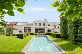 This detached, contemporary villa is situated on a spacious plot of over 1,500 m² and combines generous living spaces with a fully equipped, separate professional area. Thanks to its private entrance and air conditioning, this area can be used completely independently from the private section. This zone was originally set up as a dental practice and, due to its flexible layout, is ideal for a liberal profession, practice, consultancy, or office activity.<br /><br />The property originally dates back to 1975 and was thoroughly renovated in 2004, with a focus on comfort, functionality, and technical equipment. A living area of approximately 510 m², a well-thought-out layout, and seamless connection between the living spaces and the garden create a pleasant living experience. The high-quality Obumex kitchen is a refined and qualitatively finished part of the interior.<br /><br />A special feature of the property is the well-maintained and beautifully landscaped outdoor spaces. The heated swimming pool, sunny terraces, and fully equipped pool house with sauna, shower, and toilet create a distinct holiday feeling in the private garden. The integrated sound system on the ground floor, terrace, and in the pool house enhances this relaxed atmosphere.<br /><br />The villa is also technically well-equipped, with gas heating, a solar boiler, a heat pump for the pool, air conditioning in the master bedroom, and a central vacuum system.<br /><br />Adjacent to the property is a double garage, accessible via the driveway at the front. A second garage for one car is accessible via the rear street and provides a particularly practical additional entrance. There is also ample parking available at the front and rear.<br /><br />In short, a spacious and comfortable property where living, relaxing, and professional use come together in a natural way.