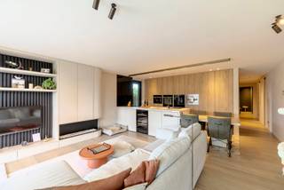 <p><strong>Instapklaar gelijkvloers appartement met carport, berging, luxe afwerking en aangelegde tuin</strong></p>
<p>Dit <strong>gelijkvloers appartement</strong> is een echte parel voor wie houdt van comfort, privacy en een hoogwaardige afwerking. Het appartement beschikt over een <strong>overdekte carport/staanplaats</strong>, een praktische <strong>berging</strong> en een volledig aangelegde tuin met overdekt terras.</p>
<p>Bij het betreden van het appartement kom je binnen in de <strong>inkomhal met gastentoilet</strong>. Van hieruit heb je toegang tot de ruime leefruimte, die stijlvol is opgedeeld in een gezellige zithoek en een volledig ingerichte eetkeuken. De leefruimte is afgewerkt met een mooie <strong>parketvloer</strong> en straalt dankzij de kwalitatieve materialen meteen warmte en klasse uit.</p>
<p>De zithoek is voorzien van een sfeervolle <strong>ethanolhaard</strong>, ideaal voor gezellige avonden. Daarnaast werd er ook gedacht aan modern wooncomfort: de <strong>geluidsinstallatie is netjes ingebouwd in het plafond</strong>, waardoor alles strak en stijlvol geïntegreerd is.</p>
<p>De <strong>eetkeuken</strong> is volledig uitgerust en afgewerkt met hoogwaardige toestellen, waaronder een microgolfoven, oven, steamer, ingebouwd koffieapparaat en een elegante wijnkast. Alles is praktisch ingedeeld en mooi ingebouwd, wat zorgt voor een verzorgde en luxueuze uitstraling.</p>
<p>Het appartement beschikt over <strong>twee ruime slaapkamers</strong>, waarvan één slaapkamer voorzien is van een ingebouwd tv-scherm. Ook aan opbergruimte is er geen gebrek: doorheen het appartement zijn er verschillende <strong>ingemaakte kasten</strong> aanwezig, waardoor alles netjes en discreet kan worden opgeborgen.</p>
<p>De centrale badkamer is uitgerust met een <strong>wastafel</strong> en een ruime <strong>inloopdouche</strong>. Verder is er een aparte wasplaats, waar wasmachine en droogkast mooi uit het zicht zijn weggewerkt.</p>
<p>Het overdekte terras zorgt ervoor dat je ook tijdens de zomermaanden aangenaam buiten kan vertoeven, met extra privacy als bijkomend voordeel.<br />Tevens is er een extra overdekte ruimte, die momenteel ingericht is met een <strong>jacuzzi en sauna</strong>.</p>
<p>De tuin is volledig aangelegd en vormt een rustige, verzorgde buitenruimte waar het heerlijk genieten is.</p>
<p>Op technisch vlak is het appartement voorzien van <strong>zonnepanelen</strong>, <strong>vloerverwarming doorheen het volledige appartement</strong>, aangesloten op centrale verwarming op aardgas. Ook op het vlak van veiligheid en gebruiksgemak is alles aanwezig: de voordeur kan vanop afstand bediend worden en aan de carport is er een <strong>camera met deurbelinstallatie</strong> voorzien.</p>
<p>Kortom: dit appartement is <strong>tot in de puntjes afgewerkt</strong>, met oog voor detail, comfort en kwalitatieve materialen. Een stijlvolle woonst waar werkelijk alles netjes werd ingebouwd en doordacht afgewerkt.</p>
<p><strong>Een pareltje voor snelle beslissers!</strong></p>