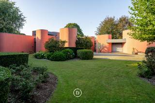 This unique architect's villa was built in 1976 and designed by architect Jan Vangheluwe. The total area of the plot is about 6000 m² with a living area of no less than 1057 m². The villa is characterised by rounded volumes and a beautiful green garden.<br /><br />Upon entering the villa, we enter a large entrance hall with guest toilet and cloakroom. <br />Central to the house is the kitchen, with storage room and cold room, which enjoys a beautiful view over the garden. Adjacent is the dining area with living room that opens onto the terrace. <br />Furthermore, there are three spacious children's bedrooms with study, a spacious bathroom, a guest bedroom with its own bathroom, a spacious master bedroom with dressing room and ensuite bathroom and a very practical laundry room.<br />The first floor includes a space that can be transformed into a hobby room or extra bedroom.<br />Finally, there is a huge multipurpose room of no less than 200 m² that can serve as office space, meeting room, reception room... <br /><br />Additional assets <br />- Double garage <br />- Spacious cellar <br />- Possibility of practising a liberal profession <br />- Plenty of parking space on the plot