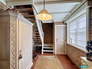 In een rustige en aangename omgeving, vlak bij het bosrijke domein rond het Kasteel d’Aertrycke, vinden we deze charmante woning terug. De woning geniet van een groene ligging en heeft tegelijk een vlotte verbinding naar diverse winkels en het openbaar vervoer. Je komt de woning binnen via de inkomhal, die toegang biedt tot het gastentoilet, de woonkamer en de vaste trap naar de eerste verdieping. De lichtrijke woonkamer biedt voldoende ruimte voor een gezellig salongedeelte en een eetplaats. Aansluitend bevindt zich de keuken, die volledig ingericht is en waar ook plaats is voor een ontbijttafel. Vanuit de keuken heb je toegang tot de garage, waar naast ruimte voor één wagen ook voorzieningen aanwezig zijn voor een wasmachine en droogkast.<br />Een grote troef op de gelijkvloerse verdieping is de lichtrijke veranda. Van hieruit geniet je van een mooi zicht op de verzorgde tuin, waardoor dit een aangename extra leefruimte vormt doorheen het jaar. Op de eerste verdieping leidt de nachthal naar drie slaapkamers, de badkamer en een praktische bergingsruimte. De badkamer is uitgerust met een ligbad, een lavabomeubel en een tweede toilet. Via een trapluik is er ook toegang tot de zolder, die extra bergruimte biedt. Achteraan de woning bevindt zich een mooi aangelegde tuin met een eerste terras aan de veranda, een moestuin en een tuinhuis met overkapping, ideaal als overdekt terras. Vooraan is er op de oprit nog plaats om een wagen te parkeren.<br />Deze woning combineert een rustige, groene ligging met praktische ruimtes en een aangename tuin. Een ideale thuis voor wie graag comfortabel woont in de nabijheid van natuur, winkels en openbaar vervoer. (sted. inl.: Vg,Wg,Gmo,Gvkr,Gvv)