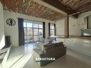 In het centrum van Merchtem bevindt zich deze ruime loft met een bewoonbare oppervlakte van ca. 133 m², ondergebracht in de voormalige Azijnbrouwerij. Het industriële karakter van het gebouw is mooi bewaard gebleven en komt onder meer tot uiting in de hoge plafonds, de authentieke plafondstructuur en de grote raampartijen.De leefruimte vormt het hart van de loft en combineert een open karakter met veel natuurlijke lichtinval. De gashaard zorgt voor extra sfeer en sluit mooi aan bij de industriële uitstraling van het geheel. Met drie slaapkamers, een EPC-label B en een centrale ligging biedt deze loft bovendien een interessante combinatie van ruimte, karakter en energiezuinigheid.IndelingEerste verdieping: Inkomhal met apart toilet, ruime en lichtrijke leefruimte, open keuken, terras, drie slaapkamers, douchekamer en badkamer met zowel bad als douche. Gelijkvloers: garage, bij aan te kopen aan €25.000 Karakteristieken- EPC-label B- Momenteel verhuurd aan € 1.175/maand- Centrale ligging in Merchtem- Zuid georiënteerd terrasEen karaktervolle loft waar de geschiedenis van het gebouw nog duidelijk voelbaar is, gecombineerd met een ruime indeling en hedendaags wooncomfort. Dankzij de drie slaapkamers, de oppervlakte van ca. 133 m² en het gunstige EPC-label B is dit een interessante eigendom voor wie op zoek is naar een ruime loft in het centrum van Merchtem. Contacteer ons via 02 460 80 46 of info@structura.be