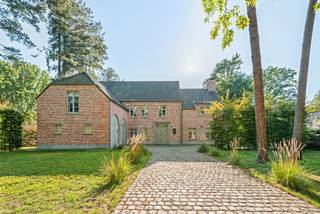 Op een van de meest gegeerde locaties van Schoten bevindt zich deze karaktervolle villa in Engelse landhuisstijl. Een oprijlaan in kasseien tussen hoogstammige bomen leidt naar de woning, die op een perceel van 2.183 m² omringd wordt door een prachtige tuin. Karakter en hedendaags comfort werden harmonieus gecombineerd op een bewoonbare oppervlakte van 615 m². Zo biedt de villa ruimte aan onder andere 5 slaapkamers, waarvan 3 met eigen dressing en ensuitebadkamer, een royale leefkeuken met ontbijthoek, een eetkamer, een bureau, een extra polyvalente ruimte, een recreatieruimte met biljart en bar, een wijnkelder en een dubbele garage.<br /><br />Gelijkvloers:<br />U betreedt de woning via een dubbele voordeur in natuurstenen omlijsting en de charmante inkomhal. Deze is afgewerkt met Belgisch blauwe hardsteen en geeft met zijn smeedijzeren trapleuning en open galerij een eerste blik op de verdieping. Van bij de eerste stap valt de authentieke Engelse sfeer op, versterkt door warm eiken parket in de leefruimtes en klassieke witte deuren met roedeverdeling.<br /><br />De hal geeft uit op de lichtrijke eetkamer, die via openslaande deuren rechtstreeks toegang geeft tot het terras en de tuin. Deze loopt verder door in de ruime living met een imposante natuurstenen schouw met open haard. Het geheel baadt in licht dankzij de hoge raampartijen.<br /><br />Het hart van de woning is de landelijke leefkeuken, met een groot kookeiland in Belgisch hardsteen en een Lacanche-fornuis, een blikvanger voor elke liefhebber van de kookkunst. De keuken loopt open over in de ontbijthoek, die dankzij de raampartijen langs drie zijden aanvoelt als een uitbouw in de tuin. Hier kunt u in elk seizoen genieten van het groen. Een praktisch bureau met ingebouwde kasten, een bergplaats en toegang tot de dubbele garage vervolledigen deze bouwlaag. Vanuit de keukenzone leidt een trap naar de wijnkelder.<br /><br />Eerste verdieping:<br />Via de trap met smeedijzeren balustrade bereikt men de ruime overloop met parket. De master bedroom beschikt over een ruime dressing en een ensuitebadkamer met bad, inloopdouche en dubbele lavabo, in klassieke stijl afgewerkt met lambrisering, metrotegels en hardsteen. Een tweede slaapkamer heeft een eigen badkamer. Een derde slaapkamer heeft een eigen dressing, een ensuitebadkamer en toegang tot een zonnig dakterras met zicht op het groen. Een praktische wasplaats met droogkast, een bergplaats en een apart toilet maken het geheel compleet.<br /><br />Ook op deze verdieping bevindt zich een bijzonder ruime kamer met hardstenen vloer, hoge plafonds en een sfeervolle kroonluchter. Dankzij het vele daglicht en de grote oppervlakte is ze veelzijdig inzetbaar, bijvoorbeeld als extra slaapkamer, speelkamer, studeerkamer of fitnessruimte.<br /><br />Tweede verdieping:<br />Op de tweede verdieping bevindt zich de recreatieruimte, met een ingebouwde bar in baksteen, een hardstenen vloer en veel daglicht via dakramen. Dit is de ideale plek voor een biljarttafel, een gezellige avond met vrienden of een speelruimte voor de kinderen. De technische ruimte en bijkomende zolderruimte vervolledigen deze bouwlaag.<br /><br />Buitenruimte:<br />De ruime tuin sluit rechtstreeks aan op de leefruimtes en vormt een oase van rust en privacy, dankzij het volwassen groen. Het royale terras aan de tuinzijde en het tuinhuis met overdekt terras nodigen uit tot een gezellig diner met vrienden of familie, terwijl de petanquebaan zorgt voor ontspanning. De dubbele garage met karaktervolle boogpoorten en de ruime oprijlaan bieden voldoende plaats voor het wagenpark.<br /><br />Technieken:<br />Ondanks de klassieke uitstraling is de villa volledig klaar voor de toekomst. Dankzij zonnepanelen, een warmtepomp, uitstekende isolatie en vloerverwarming behaalt de woning een EPC-label A. De elektrische keuring is in orde, waardoor de villa perfect instapklaar is.<br /><br />Bijzonderheden:<br />- Energiezuinig (EPC A) met zonnepanelen, warmtepomp en vloerverwarming<br />- Exclusieve villa op toplocatie<br />- 5 slaapkamers, waarvan 3 met dressing en ensuitebadkamer<br />- Leefkeuken met Lacanche-fornuis en kookeiland<br />- Extra polyvalente ruimtes, naar wens in te richten<br />- Belgisch blauwe hardsteen, eiken parket en natuurstenen schouw<br />- Zeer veel lichtinval en directe connectie met de tuin<br />- Elektrische keuring in orde, instapklaar<br /><br />Deze unieke woning in Schoten leert u het best kennen tijdens een persoonlijk bezoek. Contacteer Hillewaere en Christie's Real Estate voor een bezichtiging op afspraak en ontdek zelf het karakter, het licht en de rust van dit eigendom.