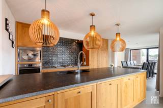 INDELING<br /><br />Bij het betreden van de woning komt u in een ruime inkomhal met vestiaire en gastentoilet. Op het gelijkvloers bevindt zich tevens de masterbedroom, uitgerust met inbouwkasten en een ensuite badkamer, wat bijdraagt aan optimaal wooncomfort. Via een glazen deur bereikt u de eetkamer, die als subtiele scheiding fungeert tussen de gezellige zithoek met pelletkachel en de maatwerkkeuken. De grote raampartijen zorgen voor een aangename lichtinval en geven rechtstreekse toegang tot het ruime terras.<br /><br />Daarnaast beschikt de woning over een praktische kelder met extra bergruimte en aansluitingen voor wasmachine en droogkast.<br /><br />Op de verdieping leidt de nachthal naar slaapkamers twee en drie en de tweede badkamer.<br /><br />De volledig omheinde tuin is voorzien van een aangenaam terras en een tuinhuis. De oprit biedt plaats aan twee wagens.<br /><br /><br />AFWERKING<br /><br />De op maat gemaakte eiken keuken is afgewerkt met een arduin werkblad en uitgerust met kwalitatieve inbouwtoestellen, waaronder een koelkast met vriesvak, aparte diepvriezer, kookplaat met gas-, inductie- en grillfunctie, geïntegreerde dampkap, stoomoven, microgolfoven, dubbele spoelbak en vaatwasser.<br /><br />Badkamer 1 beschikt over een ligbad, inloopdouche en een dubbele wastafel in meubel.<br />Badkamer 2 is ingericht met een inloopdouche, een enkele wastafel in meubel en een toilet.<br /><br />Op het gelijkvloers zijn vloertegels van 90 × 90 cm voorzien, terwijl de verdieping is afgewerkt met laminaat.