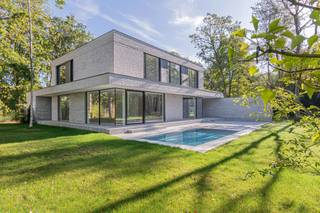 Diep verscholen in het groen, aan het einde van een discrete oprit, bevindt zich deze uitzonderlijke nieuwbouwvilla op een riant perceel van ca. 3.000 m². Dit architecturaal meesterwerk onderscheidt zich door zijn pure vormgeving, zeldzame rust en hoogwaardige materiaalkeuze — een toonbeeld van hedendaagse luxe, zonder in te boeten op warmte of leefbaarheid.<br /><br />De villa werd opgetrokken in een horizontaal metselverband met lichte, genuanceerde gevelsteen. De strakke volumewerking wordt verzacht door de overvloedige glaspartijen die van vloer tot plafond reiken. Ze zorgen niet alleen voor een adembenemende lichtinval, maar creëren ook een naadloze connectie tussen binnen en buiten. De tuin met vijver én zwembad zorgen voor verkoeling op warme dagen.<br /><br />Via de inkomhal betreed je de royale leefruimte met aangename plafondhoogte. De open leefkeuken — op maat ontworpen en voorzien van alle denkbare high-end toestellen — sluit naadloos aan op de living. Grote schuiframen openen naar het zonneterras en het strak geïntegreerde zwembad, ideaal georiënteerd op het zuiden.<br /><br />Op het gelijkvloers vinden we verder nog een gastentoilet, berging, technische ruimte en inpandige fietsenstalling — subtiel ingewerkt in de structuur van het gebouw.<br /><br />De verdieping omvat:<br /><br />- een royale slaapkamer met dressing en ensuite badkamer (inloopdouche, dubbele wastafel, vrijstaand bad)<br /><br />- twee ruime kinderkamers met ingebouwde kasten<br /><br />- een tweede badkamer en apart toilet<br /><br />Elke ruimte ademt rust, licht en verfijning.<br /><br />De villa is bovendien discreet gelegen in een doodlopende straat. Hier geniet u absolute rust en privacy in een groene oase, op wandelafstand van de prestigieuze Golf Club Keerbergen. De combinatie van deze topligging en het unieke architecturale concept maken deze eigendom ronduit zeldzaam.<br /><br />Een huis dat niet enkel ontworpen is om in te wonen, maar om in te leven.