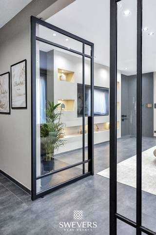 Voor meer info en foto’s, surf naar www.swevers.be – In het hart van Heusden-Zolder vinden we deze instapklare en luxueus afgewerkte halfopen woning uit 2021. Met 226 m² bewoonbare oppervlakte biedt deze gezinswoning vier ruime slaapkamers, een royale leefruimte én een multifunctionele veranda die momenteel dienstdoet als kinderdagverblijf – perfect voor wie wonen en werken wil combineren. De open leefruimte van 50 m² sluit naadloos aan op de moderne keuken van 17 m², compleet met aansluitende berging. Een extra slaapkamer op het gelijkvloers is ideaal als kantoor of praktijkruimte. De ruime veranda achteraan is lichtrijk en biedt tal van mogelijkheden voor professionele of privédoeleinden. Boven zijn er vier slaapkamers, waaronder een master van 22,5 m². De andere kamers zijn tussen 10 en 13 m² groot. De badkamer is volledig uitgerust met moderne voorzieningen. Hoewel de woning geen kelder of zolder heeft, zorgt de slimme indeling voor voldoende opbergruimte. Op het perceel van 5a 66ca geniet je van een zuidoostelijk georiënteerde tuin met zon vanaf de ochtend. Extra troeven zijn airco, alarmsysteem met camera’s, videofoon en zonnepanelen. Dankzij de centrale ligging zijn scholen, winkels, openbaar vervoer en snelwegen snel bereikbaar. Voor meer informatie, bel 011 255 155. Bron bewoonbare oppervlakte: EPC – verslag.