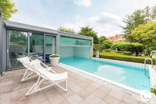 <p><span>Exclusieve architectenwoning met binnen/buitenzwembad op toplocatie in Mortsel</span></p><p><span> </span></p><p><span>Deze uitzonderlijke architectenwoning, gelegen in een gegeerde residentiële wijk nabij het Park van Mortsel, combineert tijdloze architectuur met design, functionaliteit en een uitzonderlijk wooncomfort. Een unieke eigendom voor wie op zoek is naar ruimte, licht, privacy en karakter.</span></p><p><span>De ligging vormt een absolute meerwaarde: rustig en groen, terwijl scholen, winkels, openbaar vervoer en tal van ontspanningsmogelijkheden zich op wandelafstand bevinden.</span></p><p><span> </span></p><p><span>Een bekroond architecturaal concept</span></p><p><span>Deze bijzondere woning werd ontworpen door architect Lou Jansen, die voor dit ontwerp de tweede prijs van de Robert Maskens-prijs (1980) ontving. De realisatie is het resultaat van een succesvolle samenwerking met interieurarchitect Adri Hazebroek, waarbij architectuur en interieur naadloos in elkaar overvloeien.</span></p><p><span>De woning werd in de lengte gebouwd en harmonieus geïntegreerd in de prachtig aangelegde tuin, die zich uitstrekt over twee percelen met een totale oppervlakte van ongeveer 950 m².</span></p><p><span>De solide metalen draagstructuur met een welbepaald ritme van voor- tot achteraan de woning bepaalt de verschillende leefruimtes. Zowel de individuele ruimtes als de gemeenschappelijke zones vormen samen één visueel doorlopend geheel, waarbij licht, ruimte en groen centraal staan.</span></p><p><span> </span></p><p><span>Indeling</span></p><p><span>Gelijkvloers </span><span> </span></p><p><span> </span></p><p><span>De volledig uitgeruste leefkeuken vormt zonder twijfel het hart van de woning. Vanuit de keuken geniet u van een directe toegang tot het terras en de tuin, terwijl het open ontwerp voortdurend contact houdt met de verschillende leefruimtes.</span></p><p><span>De keuken werd tot in de kleinste details doordacht. Hoogwaardige materialen en kwalitatieve toestellen zorgen voor optimaal gebruiksgemak, waaronder een inductiekookplaat, vaatwasser, oven, warmhoudlade, microgolfoven, dubbele spoelbak, ingebouwde friteuse en een duurzaam werkblad in roestvrij staal. Zelfs praktische details, zoals een discreet geïntegreerd opstapje voor de hoge kasten, werden zorgvuldig uitgewerkt.</span></p><p><span>Aansluitend bevindt zich een praktische hal met vestiaire, die rechtstreeks toegang geeft tot de wasplaats, de dubbele inpandige garage en de inkomhal. Ook de ruime kelder is vanuit de keuken gemakkelijk bereikbaar.</span></p><p><span>De kelderverdieping biedt bijzonder veel bergruimte en huisvest alle technische installaties van de woning. Daarnaast beschikt de woning over een sfeervolle, professioneel ingerichte wijnkelder waar uw wijncollectie onder ideale omstandigheden kan worden bewaard.</span></p><p><span> </span></p><p><span>Leefniveau</span></p><p><span>Via een korte trap bereikt u het centrale leefniveau, waar de architecturale kwaliteiten van deze woning volledig tot hun recht komen. De leefruimtes openen zich naar de tuin en genieten dankzij de grote glaspartijen van een overvloed aan natuurlijk licht.</span></p><p><span>De lichtrijke eetkamer vormt het centrale punt van deze verdieping en wordt langs de zijkant volledig omringd door groen. Aansluitend bevindt zich een eerste elegant salon met een prachtig zicht op de aangelegde tuin, de terrassen en het zwembad. Deze ruimte is ideaal om gasten te ontvangen of in alle rust te genieten van een aperitief, terwijl de groene omgeving een unieke, zuiderse sfeer creëert.</span></p><p><span>Verder op het leefniveau bevindt zich een tweede, meer intieme zithoek met een gezellige open haard. Deze tv- en familieruimte sluit naadloos aan op de bureauruimte, die jarenlang dienstdeed als bureau- en ontvangstruimte. Vandaag biedt deze veelzijdige ruimte tal van mogelijkheden als thuiskantoor, speelruimte of extra leefruimte. Dankzij de afsluitbare indeling geniet u hier van een perfecte balans tussen verbondenheid en privacy.</span></p><p><span> </span></p><p><span>Nachtniveau</span></p><p><span>De masterbedroom bevindt zich op een afzonderlijk niveau van de woning en vormt een volledig private suite.</span></p><p><span>Deze ruime slaapkamer beschikt over een praktische dressing en een luxueuze en-suite badkamer, uitgerust met een bubbelbad, een ruime inloopdouche en een stijlvol lavabomeubel.</span></p><p><span>Aansluitend bevindt zich een gezellig privéterras waar u in alle rust kunt genieten van een koffie in de ochtend of een ontspannen avond met zicht op het omliggende groen.</span></p><p><span>Vanuit dit niveau heeft u bovendien toegang tot de wellnessruimte met sauna, fitnessruimte en het verwarmde binnenzwembad dat naadloos overloopt in het buitenzwembad.</span></p><p><span> </span></p><p><span>Bovenste verdieping</span></p><p><span>Op de bovenste verdieping bevinden zich twee volwaardige slaapkamers, een aparte gastenkamer en een tweede badkamer.</span></p><p><span>De tweede badkamer is praktisch ingericht met een douche en een stijlvol lavabomeubel en vormt een aangename meerwaarde voor de slaapkamers en eventuele gasten.</span></p><p><span>De gastenkamer beschikt over een extra zitruimte in de nok van de woning. Dankzij de bijzondere lichtinval is dit een ideale plek om rustig te lezen, te ontspannen of te genieten van een moment voor uzelf. De architecturale vormgeving van de nok zorgt hier voor een bijzonder sfeervolle ruimte met karakter.</span></p><p><span> </span></p><p><span>Buitenleven</span></p><p><span>ook buiten werd niets aan het toeval overgelaten.</span></p><p><span>de fraai aangelegde tuin beschikt over meerdere zonneterrassen, een verwarmd binnen- en buitenzwembad en een prachtige groene pergola achteraan het perceel, waardoor u zich meteen in zuid-frankrijk waant.</span></p><p><span>een ruime tuinberging biedt voldoende plaats voor al het tuinmateriaal. de tuin werd bovendien bijzonder verzorgd aangelegd en is dankzij de doordachte inrichting aangenaam te onderhouden.</span></p><p><span>een extra troef is het tweede perceel achteraan de woning, dat bereikbaar is via zowel de lusthovenlaan als de vernieuwde Edmond Thieffrylaan. het achterste gedeelte van het perceel ligt bovendien op bouwgrond, wat extra potentieel biedt.</span></p><p><span> </span></p><p><span>Comfort en technieken</span></p><p><span>doorheen de jaren werd de woning voortdurend gemoderniseerd met bijzondere aandacht voor kwaliteit, duurzaamheid en energiezuinigheid. dit resulteert in een gunstig EPC-label b.</span></p><p><span> </span></p><p><span>De woning beschikt onder meer over:</span></p><p><span>·Zonnepanelen</span></p><p><span>·Vloerverwarming</span></p><p><span>·Airconditioning</span></p><p><span>·Luchtverwarming gestuurd door een recente gasketel</span></p><p><span>·Gedeeltelijk zonwerend glas</span></p><p><span>·Glass Heating-beglazing op geselecteerde ramen</span></p><p><span>·Verwarmd binnen- en buitenzwembad met warmtepomp</span></p><p><span>·Dubbele inpandige garage</span></p><p><span>·Ruime kelder en wijnkelder</span></p><p><span> </span></p><p><span>Een unieke woonbeleving</span></p><p><span>Deze uitzonderlijke architectenwoning combineert bekroonde architectuur met hedendaags comfort, hoogwaardige afwerking en een unieke beleving van binnen- en buitenruimte.</span></p><p><span>Een zeldzame opportuniteit voor wie op zoek is naar een exclusieve woning op een toplocatie in Mortsel, waar kwaliteit, ruimte, natuur en luxe perfect samenkomen.</span></p><p><span>Deze woning moet u voelen en beleven. </span></p><p><span>Maak een afspraak op www.coprimmo.be of 03/449.49.77</span></p><p><span> </span></p><p><span> </span></p>