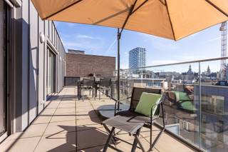 Deze instapklare penthouse is gelegen in de Lange Sint-Annastraat, een karaktervolle straat in het hart van Antwerpen, op het kruispunt van het Eilandje, de universiteitswijk en het historische centrum. Stijlvolle winkels, kwalitatieve horeca en culturele hotspots bevinden zich op wandelafstand, net als de Meir, Groenplaats en Grote Markt. Dankzij deze centrale ligging geniet u van het bruisende stadsleven, terwijl u bovenaan het gebouw in alle rust thuiskomt. Zowel openbaar vervoer als belangrijke invalswegen zijn vlot bereikbaar.<br /><br />Het appartement bevindt zich op de bovenste verdieping van een recente en verzorgde residentie. De lichtrijke leefruimte vormt het hart van het appartement en geeft via grote raampartijen toegang tot twee ruime zonneterrassen aan weerszijden. Dit zorgt de hele dag door voor overvloedig natuurlijk licht en een aangenaam panoramisch uitzicht over de stad. Aansluitend aan de leefruimte bevindt zich een aparte bureauruimte, ideaal als thuiswerkplek of in te richten als derde slaapkamer.<br /><br />De keuken is volledig uitgerust met kwalitatieve toestellen en een ruim werkblad, perfect voor wie graag kookt en gasten ontvangt. Verder beschikt het appartement over twee ruime slaapkamers, een modern afgewerkte badkamer met ligbad, inloopdouche en dubbel lavabomeubel, een apart gastentoilet en een praktische (was) berging. <br />Een privatieve kelderberging en gemeenschappelijke fietsenberging zijn inbegrepen. De aankoop van een ondergrondse autostaanplaats is mogelijk.