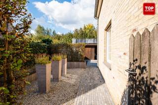 Deze instapklare woning is gelegen in een rustige, kindvriendelijke woonwijk en bevindt zich in een doodlopende straat. <br />De woning zich op slechts een steenworp van alle nodige voorzieningen zoals scholen, winkels en openbaar vervoer. Dankzij de nabijheid van de R4 geniet u van een uitstekende verbinding van en naar Gent en omliggende gemeenten.<br /><br />Bij het betreden van de woning komt u binnen in de inkomhal met apart toilet. Verder gaat u via de inkomhal naar de lichtrijke woonkamer, de inpandige garage (met sectionale poort) en de bovenverdieping. <br />De ruime leefruimte baadt in het natuurlijke licht en kijkt uit op de groene tuin, aansluitend aan de woonkamer bevindt zich de volledig uitgeruste keuken, voorzien van alle hedendaagse comfort en met directe toegang tot het aangelegd terras met recente zonneluifel. De woning is voorzien van rolluiken, ook boven aan de dakramen, een waterontkalker en centraal stofzuigersysteem.<br /><br />De tuin is onderhoudsvriendelijk aangelegd. Achteraan de tuin staat een praktisch tuinhuis, uitgerust met zonnepanelen. Extra troef: de tuin grenst aan een groenzone, wat het uitzicht en de privacy ten goede komt.<br /><br />Op de eerste verdieping bevinden zich drie volwaardige slaapkamers (allemaal met parket voorzien) en een badkamer met zowel een ligbad als een douche. Daarnaast beschikt de woning over een ruime zolder, ideaal voor extra bergruimte.<br /><br />Beschikbaar uiterlijk 30/6/26.<br /><br />Contacteer Top Vastgoed voor een bezoek op 0475 700 700.