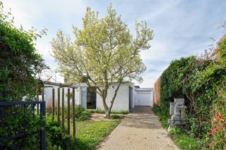 <em>Deze woning in Sint-Truiden is een uitzonderlijk voorbeeld van een kunstenaarswoning waarin architectuur, beeldende kunst en landschap in volledige symbiose samenkomen. Ontworpen in 1961 door architect Adolf Nivelle, in nauwe dialoog met de toenmalige bouwheer en kunstenaar Toon Vanmechelen, overstijgt deze woning het louter functionele wonen. Het is een plek waar denken, maken en leven samenkomen in één coherent geheel, gedragen door een sterke modernistische visie met uitgesproken brutalistische accenten.</em><br /><br /><strong>De signatuur van adolf nivelle</strong><br />Adolf Nivelle behoort tot een generatie architecten die zich bewust afzette tegen ornament en oppervlakkigheid, en resoluut koos voor een architectuur van essentie en structuur. Zijn werk wordt gekenmerkt door een helder constructief denken, een consequente materialiteit en een bijzondere gevoeligheid voor ruimte, licht en inplanting. In deze woning komt die visie tot volle maturiteit.<br />Nivelle benadert architectuur als een totaalkunstwerk waarin elk element — van dragende structuur tot detailafwerking — deel uitmaakt van een groter geheel. De strakke geometrie, de ritmiek van horizontale lijnen en de zorgvuldige positionering op het perceel tonen een architect die niet enkel bouwt, maar componeert. De woning is geen object op zich, maar een ruimtelijke ervaring die zich ontvouwt in relatie tot haar omgeving.<br /><br /><strong>De kunstenaar als medeschepper</strong><br />De aanwezigheid van kunstenaar Toon Vanmechelen als bouwheer en mededenker geeft deze woning een extra gelaagdheid. Dit is geen klassieke samenwerking waarbij kunst pas nadien wordt toegevoegd, maar een intrinsieke verweving van kunst en architectuur vanaf de eerste schets. De woning werd opgevat als een leef- en werkplek waarin artistieke expressie een vanzelfsprekende plaats krijgt.<br />De beeldhouwwerken en artistieke ingrepen, zowel in de tuin als in de overgangszones van de woning, functioneren niet als decoratie maar als ruimtelijke ankerpunten. Ze begeleiden de beweging doorheen het huis, creëren accenten en versterken de beleving van schaal en perspectief. De patio en voortuin worden zo verlengstukken van het atelier, terwijl het interieur een subtiele galerie wordt waarin kunst en dagelijks leven elkaar ontmoeten.<br /><br /><strong>Architectuur, kunst en tuin in dialoog</strong><br />Wat deze woning bijzonder maakt, is de continue dialoog tussen de rationele helderheid van de architectuur, de expressieve kracht van de kunst en de verstilde aanwezigheid van de tuin. Waar Nivelle structuur, rust en orde brengt, voegt Vanmechelen een meer intuïtieve, sculpturale laag toe. De tuin vormt daarin geen decor, maar een wezenlijk onderdeel van de woonbeleving.<br /><br />Met grote zorg werd het domein aangelegd en onderhouden, niet volgens een strak Frans schema, noch volgens een uitgesproken Engelse traditie, maar veeleer vanuit het gevoel en de intuïtie van de eigenaar. Die persoonlijke benadering geeft de buitenruimte een bijzondere zachtheid en vanzelfsprekendheid. De bloei begint vroeg in het seizoen met de magnolia, waarna de tuin zich verder ontvouwt in een bijna continue opeenvolging van kleuren, texturen en geuren. Doorheen het jaar blijft zij in beweging, levendig en toch sereen.<br /><br />Eens op het domein komt men in een oase van rust terecht, waarin de tuin een hoofdrol speelt. Grote glaspartijen kaderen zichten op het groen en op de aanwezige sculpturen, waardoor binnen en buiten, kunst en natuur, voortdurend met elkaar verweven blijven. De tuin verzacht de kracht van de architectuur, zonder haar te verzwakken, en versterkt tegelijk het contemplatieve karakter van de woning.<br /><br /><strong>Een leefomgeving voor makers</strong><br />De indeling en ruimtelijke opbouw van de woning verraden haar oorsprong als kunstenaarswoning. Naast de genereuze leefruimtes en slaapkamers is er expliciet ruimte voorzien voor creatie, reflectie en experiment. De aanwezigheid van een atelier en de flexibele invulling van verschillende ruimtes maken het geheel bijzonder geschikt voor wie wonen en werken wil combineren.<br />Tegelijk blijft de woning in haar opzet bijzonder helder en functioneel. De circulatie is logisch, de ruimtes zijn goed geproportioneerd en het daglicht wordt op een doordachte manier doorheen het huis geleid. Dit zorgt voor een leefkwaliteit die, ondanks de uitgesproken architecturale identiteit, bijzonder comfortabel en vanzelfsprekend aanvoelt.<br /><br /><strong>Een erfstuk met toekomst</strong><br />Hoewel de woning vandaag een energetische update vraagt, blijft de architecturale basis uitzonderlijk waardevol. De robuuste structuur en de sterke ontwerpvisie bieden een solide kader voor een hedendaagse interpretatie, waarbij duurzaamheid en comfort kunnen worden geïntegreerd zonder het karakter aan te tasten.<br /><br />Deze woning is meer dan een plek om te wonen. Het is een erfstuk waarin architectuur, kunst en landschap elkaar versterken — een omgeving die inspireert, vertraagt en verdiept. Een zeldzame kans voor wie op zoek is naar een woning met een verhaal, een ziel en een uitgesproken identiteit.<br /><br /><strong>Meer ontdekken?</strong><br />Wil je graag thuiskomen in deze uitzonderlijke woning?<br />Contacteer mij dan snel voor meer info of een persoonlijk bezoek ter plaatse!<br /><br /><em>De vermelde oppervlaktes zijn slechts indicatief. Katrien Wouters - creating IMMOtions kan niet verantwoordelijk gesteld worden voor de juistheid van de aan haar verstrekte gegevens.  </em>