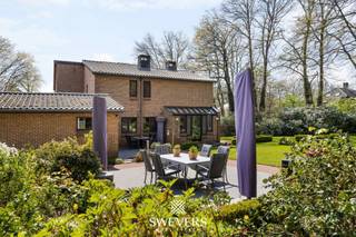 Voor meer info en foto’s, surf naar www.swevers.be – Deze ruime open bebouwing aan de Koerselsesteenweg 146 in Beringen combineert comfortabel wonen met professionele mogelijkheden. Dankzij aparte ingangen voor het privé- en praktijkgedeelte is de woning ideaal voor een zelfstandige activiteit aan huis, maar ook geschikt voor kangoeroewonen. De woning dateert van 1980 en werd doorheen de jaren gericht vernieuwd, met onder meer een nieuw pannendak, gerenoveerde living en keuken, vernieuwde condensatieketel, drie nieuwe Veluxramen en zonnepanelen uit 2023. Met een bewoonbare oppervlakte van 340 m² is er bijzonder veel ruimte. Op het gelijkvloers bevinden zich een woonkamer met eetkamer van samen 46 m², een keuken van 16,40 m², bureau en apart toilet. Het praktijkgedeelte omvat een wachtruimte, consultatieruimte, archief/doka en eigen toilet. Daarnaast zijn er een inpandige garage van 42 m² en een ruime berging. De eerste verdieping telt vier slaapkamers van 12,5 tot 22 m², waarvan één met terras en één met ingemaakte kasten. Verder zijn er een badkamer en apart toilet. De kelder van 44 m² zorgt voor extra bergruimte. Het perceel van 37a 75ca beschikt over een groen aangelegde tuin met meerdere terrassen en tuinhuisjes. Er is parkeerruimte voor 8 à 10 wagens. Scholen, openbaar vervoer en de snelweg zijn vlot bereikbaar. Extra troeven zijn het alarmsysteem, rolluiken, zonnewering en een beveiligde deur. Voor meer informatie, bel 011 255 155. Bron bewoonbare oppervlakte: EPC – verslag.