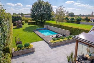 <p>Aan de Steenweg Weelde 68 in Poppel vinden we deze ruime en sfeervolle gezinswoning op een perceel van 1.717 m². De woning werd door de jaren heen goed onderhouden en op verschillende vlakken vernieuwd. Zo werden de technieken aangepakt en werd o.a. geïnvesteerd in zonnepanelen en een laadpaal.</p>
<p>Met vier slaapkamers, ruime leefruimtes, een grote zolder, inpandige garage en een prachtig aangelegde tuin met verwarmd zwembad biedt deze woning volop ruimte en comfort voor het hele gezin.</p>
<p><strong>Sfeervol wonen<br /></strong>De woonkamer straalt een warme, huiselijke sfeer uit. De parketvloer, originele deuren, sierlijsten en houtkachel zorgen voor een mooie combinatie van sfeer en authenticiteit.</p>
<p>Via de authentieke deuren bereikt u de eetkamer. Dankzij de grote schuifpui staat deze ruimte rechtstreeks in verbinding met de achtertuin. De grote raampartijen zorgen bovendien voor een aangename lichtinval.</p>
<p>Daarnaast beschikt de woning over een praktische achterinkom met een toilet en een extra berging.</p>
<p><strong>Ruime, complete keuken<br /></strong>De keuken is voorzien van alle nodige comfort, waaronder een 5-pits inductiekookplaat.</p>
<p>Vanuit de keuken heeft u toegang tot de voorraadberging en de kelder. De kelder is droog en volledig betegeld.</p>
<p>Aansluitend aan de keuken bevindt zich aan de voorzijde van de woning het bureau. Deze ruimte beschikt over openslaande deuren en ingebouwde kasten in dezelfde stijl als de keuken. Een veelzijdige ruimte die perfect kan dienen als thuiswerkplek of hobbyruimte.</p>
<p><strong>Vier slaapkamers, badkamer en wasruimte<br /></strong>Op de eerste verdieping bevinden zich vier volwaardige slaapkamers. De master bedroom beschikt over een dressing met ingebouwde kasten.</p>
<p>De badkamer is uitgerust met een inloopdouche, dubbele wastafel en ligbad. Het toilet bevindt zich afzonderlijk.</p>
<p>Ook de praktische wasruimte bevindt zich op deze verdieping en is voorzien van aansluitingen voor wasmachine en droogkast en er is een wastafel.</p>
<p><strong>Zolder met mogelijkheden<br /></strong>De zolder biedt heel wat potentieel. Afhankelijk van de wensen van de nieuwe eigenaar kan deze ruimte verder worden ingericht als extra slaapkamers met badkamer, hobbyruimte of andere multifunctionele ruimte.</p>
<p>Er is reeds een afvoer voorzien, wat mogelijkheden biedt voor een toekomstige verbouwing.</p>
<p><strong>Garage en extra bergruimte<br /></strong>De woning beschikt over een inpandige garage. Via een vlizotrap bereikt u bovendien een praktische bergzolder, ideaal voor extra opslag.</p>
<p><strong>Een tuin als verlengstuk van de woning<br /></strong>De fraai aangelegde tuin is zonder twijfel een van de grote troeven van deze woning. De groene omgeving biedt veel privacy en verschillende plekken om te ontspannen.<br /><br />De overkapping aan de woning biedt een aangename plek om beschut van de tuin te genieten.</p>
<p>Het verwarmde zwembad zorgt tijdens de warme maanden voor een heerlijk vakantiegevoel in eigen huis. Dankzij de warmtepomp kan het zwembad aangenaam worden verwarmd en met de aanwezige buitendouche is ook extra comfort voorzien.</p>
<p>De tuin beschikt daarnaast over verschillende fruitbomen en struiken, waaronder peren, appels, pruimen, noten en druiven. Voor de kinderen is er een speeltoestel en ook een kippenren maakt deel uit van het geheel.</p>
<p>Daarnaast werd in 2020 een praktisch bijgebouw geplaatst, ideaal voor het stallen van bijvoorbeeld tuinmateriaal.</p>
<p><strong>Troeven op een rij:</strong><br />- Verwarmd zwembad met warmtepomp en buitendouche<br />- Ruime, groene tuin met veel privacy<br />- Zonnepanelen en laadpaal<br />- Sfeervolle woonkamer met parketvloer, originele deuren, sierlijsten en houtkachel<br />- Zolder met uitbreidingsmogelijkheden<br />- Inpandige garage en extra bergzolder<br />- Vernieuwde technieken en diverse recente investeringen<br /><br />Vermelde oppervlakten zijn indicatief. Oppervlakte conform EPC.</p>
