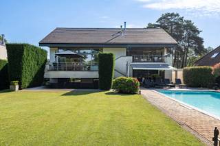 <p><strong>Exclusieve split-levelvilla met 5 slaapkamers, zwembad en prachtig aangelegde tuin</strong></p>
<p>Wie op zoek is naar een woning met <strong>karakter</strong>, <strong>uitzonderlijke volumes</strong> en een <strong>unieke woonbeleving</strong>, zal onmiddellijk gecharmeerd zijn door deze <strong>indrukwekkende split-levelvilla</strong>. Dankzij haar <strong>speelse architectuur</strong>, <strong>royale leefruimtes</strong> en <strong>prachtige buitenomgeving</strong> biedt deze eigendom een <strong>zeldzame combinatie van luxe, comfort en functionaliteit</strong>.</p>
<p>Vanaf het eerste moment valt de <strong>bijzondere indeling</strong> van de woning op. De verschillende niveaus creëren een natuurlijke scheiding tussen wonen, slapen, werken en ontspannen, terwijl de open verbindingen zorgen voor een aangenaam gevoel van <strong>ruimte en licht</strong>. <strong>Grote raampartijen</strong> laten het daglicht overvloedig binnenstromen en bieden op verschillende plaatsen een prachtig zicht op de tuin en de omliggende <strong>groene omgeving</strong>.</p>
<p>Het absolute middelpunt van de woning is zonder twijfel de <strong>uitzonderlijk ruime woonkamer</strong> van maar liefst circa <strong>83 m²</strong>. Dankzij de directe toegang tot het <strong>ruime terras</strong> vloeien <strong>binnen- en buitenleven</strong> naadloos in elkaar over.</p>
<p>Een niveau hoger bevindt zich de <strong>ruime leefkeuken</strong> die perfect aansluit op de aangename eetruimte. Deze combinatie vormt het <strong>kloppende hart van het huis</strong> waar koken, tafelen en samenzijn centraal staan.</p>
<p>De villa telt maar liefst <strong>vijf volwaardige slaapkamers</strong>, verspreid over verschillende niveaus. Hierdoor geniet ieder gezinslid van voldoende <strong>privacy en comfort</strong>. De <strong>hoofdslaapkamer van circa 33 m²</strong> vormt een echte <strong>privésuite</strong> met een royaal gevoel van ruimte en rust.</p>
<p>Verder beschikt de woning over een <strong>ruime badkamer</strong> met ligbad en douche, meerdere sanitaire voorzieningen en een afzonderlijke wasruimte, wat het dagelijkse comfort aanzienlijk verhoogt.</p>
<p>Voor wie van thuis uit werkt of extra ruimte nodig heeft voor een praktijk, hobby of creatieve activiteiten, biedt de woning een <strong>uitzonderlijk ruime kantoorruimte</strong> van ongeveer <strong>31 m²</strong>.</p>
<p>Buiten ontvouwt zich een ware <strong>oase van rust en privacy</strong>. De <strong>grote, perfect onderhouden tuin</strong> vormt een groene omgeving waar jong en oud het hele jaar door kunnen genieten. Centraal in de tuin ligt het <strong>zwembad</strong>, dat tijdens de zomermaanden garant staat voor <strong>ontspanning</strong> en een echt <strong>vakantiegevoel in eigen huis</strong>. De verschillende terrassen rond de woning bieden op elk moment van de dag een aangename plek om te genieten van de zon of de schaduw.</p>
<p>De architectuur van deze split-levelvilla zorgt niet alleen voor een bijzonder ruimtelijk gevoel, maar geeft de woning ook een <strong>unieke uitstraling</strong> die haar onderscheidt van klassieke villa's.</p>
<p><strong>Troeven op een rij</strong></p>
<p>✔ Exclusieve split-levelarchitectuur<br />✔ 5 ruime slaapkamers<br />✔ Ruime kantoorruimte<br />✔ Verschillende terrassen<br />✔ Grote zolder met uitbreidingsmogelijkheden<br />✔ Perfect onderhouden en aangelegde tuin<br />✔ Verwarmd zwembad<br />✔ Veel natuurlijke lichtinval</p>
<p><strong>Een bezoek zal u zonder twijfel overtuigen van de uitzonderlijke kwaliteiten van deze eigendom.</strong></p>