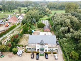 Dit gebouw met woon- en handelsfunctie ligt op een goede zichtlocatie en beschikt over een private parking aan de straatkant. De totale oppervlakte van de percelen bedraagt 1ha 11a 08ca. Het hoofdgebouw bestaat enerzijds uit een gelijkvloerse winkel met een oppervlakte van 200 vierkante meter en anderzijds uit een duplex appartement met een oppervlakte van 300 vierkante meter.<br />Naat het winkelgedeelte zijn er op het gelijkvloers een apart toilet, een kleine berging, een grote berging met functionerende koelcel, en een polyvalente ruimte met voorzieningen om de in te richten als studio (televisieaansluiting, wateraanvoer en -afvoer, elektriciteit).<br /><br />Het woongedeelte is zowel apart toegankelijk als via de winkel.<br />Het appartement baadt in het zonlicht. De grote raampartijen aan voor- en achterkant, het hoge plafond met mezzanine en de glazen deuren creëren een ruimtelijk gevoel en brengen extra lichtinval binnen. De ruime living met open keuken wordt verwarmd met vloerverwarming. Op het eerste verdiep bevinden zich verder een apart toilet, een slaapkamer met annex dressing (met aanwezige voorziening voor een badkamer), een tweede slaapkamer/bureau en een grote berging met de chauffageketel, een lavabo en de aansluiting voor een wasmachine.<br />Het volledige plat dak aan de keuken kan gebruikt worden als terras.<br /><br />Op het tweede verdiep bevindt zich links de masterbedroom met badkamer en ruimte voor een dressing. Rechts liggen 2 slaapkamers (met ingebouwde kasten, burelen en een wastafel), een apart toilet en een douchekamer.<br />De totale bruikbare vloer oppervlakte bedraagt 334m2 (bron EPC)<br /> <br />De betegelde serre grenst aan het hoofdgebouw. De kweekserre grenst aan een vrijstaand bijgebouw met verschillende bureelruimtes.<br /><br />Omwille van de ligging in agrarisch gebied, moet het pand een agrarische functie behouden. Mits functiewijziging kan het ook aangewend worden als paardenhouderij, manège, dierenasiel, dierenartsenpraktijk, jeugdlogies, tuinaanlegbedrijf, kinderboerderij, centrum voor dierentherapie, een instelling waar personen al dan niet tijdelijk verblijven bij wijze van therapie, onderwijs, opleiding of voorbereiding op de reguliere arbeidsmarkt die onder meer land- en tuinbouwactiviteiten uitoefenen of aan land- en tuinbouw verwante activiteiten uitoefenen.