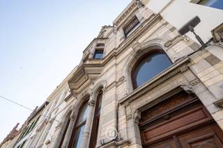 Dit prestigieuze eclectische herenhuis, gelegen in de winkelstraat van Oudenaarde, biedt een unieke kans voor ondernemers die op zoek zijn naar een uitzonderlijk handelspand met een luxueuze uitstraling. Met zijn iconische gevel, één van de meest herkenbare en karaktervolle gevels van de stad, geniet dit pand van een ongeëvenaarde zichtbaarheid en grandeur. De unieke architectuur en de hoogwaardige afwerking zorgen ervoor dat deze eigendom niet alleen een uitstekende commerciële ruimte biedt, maar tevens een stijlvolle woongelegenheid in het hart van de stad.<br /><br />De begane grond is volledig ingericht als een ruime en functionele commerciële ruimte die perfect geschikt is voor diverse doeleinden, zoals een winkel, een showroom of een atelier. De afwerking met granieten elementen draagt bij aan de luxueuze uitstraling, terwijl de royale inkomhal met massief marmeren accenten bezoekers op een indrukwekkende manier verwelkomt. Daarnaast beschikt deze verdieping over een apart gastentoilet, een bijkeuken, een technische ruimte en een kluis. Twee trappen bieden toegang tot ruime kelders, die ideaal kunnen dienen als opslagruimte of voorraadbeheer.<br /><br />Het commerciële gedeelte heeft directe toegang tot een sfeervolle binnenkoer, wat niet alleen een aangename werkruimte creëert, maar tevens een bijkomende troef is voor zowel klanten als medewerkers. Bovendien beschikt het pand over een zonnige tuin, een dakterras en een ruime garage met carport, die toegankelijk zijn via een achterliggende straat. Deze extra voorzieningen vormen een onschatbare meerwaarde voor een handelspand in het centrum van Oudenaarde en verhogen het gebruiksgemak voor zowel professioneel als privégebruik.<br /><br />Naast de commerciële mogelijkheden biedt dit eigendom eveneens een ruime en stijlvolle woongelegenheid, waarin authentieke charme en hedendaags comfort harmonieus samenkomen. De imposante inkomhal leidt naar een elegant salon met open haard, een eetkamer en een volledig uitgeruste keuken met een praktische berging. Op de tussenverdieping bevinden zich de wasplaats en de eerste badkamer. De eerste en tweede verdieping omvatten samen vier ruime slaapkamers en twee badkamers, waardoor deze woning bijzonder geschikt is voor ondernemers die hun professionele activiteiten wensen te combineren met een luxueus en comfortabel privéleven.<br /><br />Dankzij de uitzonderlijke ligging, de stijlvolle afwerking en de historische uitstraling vormt dit pand een unieke opportuniteit voor wie op zoek is naar een prestigieus handelspand met woonst in het centrum van Oudenaarde. De combinatie van een exclusieve commerciële ruimte met een ruime en comfortabele woongelegenheid biedt niet alleen een uitstekende zichtbaarheid en bereikbaarheid, maar verzekert ook een ongeëvenaarde uitstraling voor iedere onderneming. Voor meer informatie of een bezichtiging kunt u contact met ons opnemen.