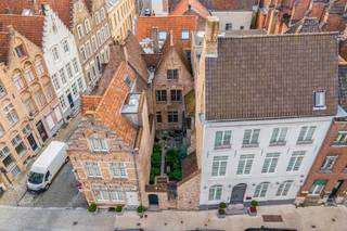 In het hart van Brugge, verscholen achter een discreet muurtje met toegangspoort, bevindt zich dit uitzonderlijke gotische herenhuis uit 1550. Een bijzonder stukje Brugs erfgoed, met één van de slechts twee bewaarde originele houten gevels in de stad. Authentiek, karaktervol en bovenal uniek.<br /><br />De ligging is al even bijzonder als het pand zelf. Vanuit de Vlamingstraat wandelt u zo naar het Belfort, de Markt en de vele restaurants, boetieks en culturele trekpleisters die de Brugse binnenstad rijk is. Een uitzonderlijke locatie voor wie volop van het stadsleven wil genieten en tegelijk waarde hecht aan privacy en rust.<br /><br />Binnen zet de historische grandeur zich moeiteloos voort. Robuuste houten plafondbalken, fraaie parketvloeren, authentieke muurnissen en een sfeervolle open haard geven de woonvertrekken een warme en tijdloze uitstraling.<br /><br />De woning omvat een eetruimte met keuken, een karaktervolle salon met open haard, twee slaapkamers met de mogelijkheid om een derde slaapkamer te creëren, en een badkamer, verdeeld over het gelijkvloers en twee verdiepingen.<br /><br />Wie historisch karakter graag combineert met hedendaags wooncomfort, vindt hier bovendien heel wat mogelijkheden. Zo kan de bestaande keuken worden omgevormd tot een moderne open keuken door onder meer het lage tussenmuurtje weg te nemen. Ook de badkamer kan volledig worden vernieuwd tot een eigentijdse badkamer met douche, lavabo en toilet. Rond de karaktervolle eiken spiltrap kan bovendien een stijlvolle stalen leuning worden geplaatst, als hedendaags accent dat mooi contrasteert met de authentieke elementen van de woning.<br />Een absolute blikvanger is de prachtige erker op de eerste verdieping, vanwaar u uitkijkt over de charmant aangelegde binnentuin.<br /><br />Ook ondergronds verrast deze woning. De ruime middeleeuwse kelder biedt tal van mogelijkheden en vormt opnieuw een bijzonder authentiek onderdeel van het geheel.<br />Buiten vormt de beschutte binnentuin een groene oase midden in de stad. Hier geniet u in alle privacy van rust, groen en de unieke sfeer van een eeuwenoud Brugs herenhuis.<br /><br />Een zeldzame stadsparel voor wie op zoek is naar méér dan een woning: beschermd erfgoed, een uitzonderlijke houten gevel te Kortewinkel, een authentiek interieur en een topligging komen hier samen in een eigendom met een werkelijk uniek karakter.