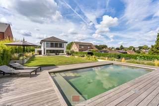 Wonen waar elke dag als vakantie voelt<br /><br />Sommige woningen bieden comfort. Andere bieden ruimte. En dan zijn er plekken waar alles samenkomt: hedendaags wonen, rust en een uitzicht dat je niet snel vergeet.<br />Op een royaal perceel van circa 910 m² ligt deze moderne en energiezuinige woning van circa 177 m² bewoonbare oppervlakte, met een weids panorama over het Limburgse Heuvelland. <br /><br />De open leefkeuken en de aangrenzende eetruimte vormen het hart van het huis. Via schuifpuien loopt de leefruimte direct over in het terras en de tuin, waardoor binnen en buiten op een natuurlijke manier in elkaar overvloeien. Op de bovenverdieping bevinden zich drie kamers, twee badkamers en een separaat toilet. De ruime mastersuite beschikt over een eigen badkamer en walk-in closet. Daarnaast is er een tweede slaapkamer en een derde kamer die momenteel ingericht is als tv- en ontspanningsruimte, maar eenvoudig kan worden omgevormd tot volwaardige derde slaapkamer.<br /><br />Ook op het gebied van techniek is aan alles gedacht. De geothermische warmtepomp, vloerverwarming en passieve koeling zorgen het hele jaar door voor een aangenaam binnenklimaat. De zonnepanelen dragen bij aan een energiezuinige werking, terwijl de automatische toegangspoort, slimme verlichting en camerabeveiliging extra gemak en privacy bieden. Buiten wordt het vakantiegevoel compleet. De mediterrane beplanting, verschillende terrassen, de fraai aangelegde zwemvijver en vooral het unieke, weidse uitzicht over het glooiende landschap maken dit een plek waar je iedere dag opnieuw tot rust komt. <br /><br />En misschien is dat precies wat deze woning zo bijzonder maakt. Je hoeft niet ver te reizen om er even helemaal uit te zijn. <br /><br />Modern wonen. Eindeloos uitzicht. Elke dag een beetje vakantie.<br /><br />Teuven – wonen midden in het Heuvelland<br /><br />De woning bevindt zich in het pittoreske Teuven, een karaktervol dorp in de gemeente Voeren, midden in het prachtige landschap van de Voerstreek. De omgeving wordt gekenmerkt door glooiende heuvels, uitgestrekte weilanden, bossen en de vallei van de Gulp en vormt daarmee een bijzondere woonomgeving voor liefhebbers van rust, natuur, wandelen en fietsen.<br />Teuven beschikt over een charmante dorpskern met de historische Sint-Pieterskerk als herkenningspunt en een verrassend levendig horeca-aanbod. Vanuit het dorp vertrekken talrijke wandel- en fietsroutes door het heuvelachtige landschap en de omliggende Voerense bossen.<br />Ondanks de landelijke ligging zijn verschillende voorzieningen en omliggende dorpen vlot bereikbaar. Ook de nabijheid van de Nederlandse grens is een belangrijke troef. Slenaken, Aubel en ’s-Gravenvoeren liggen op korte afstand, terwijl ook Maastricht, Luik en Aken goed bereikbaar zijn.<br />Een omgeving die uitblinkt in rust, groen, ruimte en landelijke charme, maar tegelijkertijd uitstekend verbonden blijft met de omliggende dorpen en steden.<br /><br />Bezichtig deze woning ook digitaal en 'loop' zelf door de woning. Kijk daarvoor op onze website of via: my.matterport.com/show/?m=D3ATBZQCmxw<br /><br />INDELING<br /><br />Gelijkvloers:<br /><br />- Inkomhal met vestiaire kasten;<br />- Gastentoilet met lavabo met onderkast;<br />- Betonnen trap (kan desgewenst naar smaak verder worden afgewerkt);<br />- Ruime living met directe toegang tot de eetkamer en keuken;<br />- Eetkamer met zicht op de prachtig aangelegde tuin;<br />- Complete keuken met allemaal Siemens toestellen (vaatwasser, combi-oven, inbouwkoffiezet, oven, XXL frigo, Novy inductieplaat met ingebouwde dampkap), afgietbak (Franke) op apart kastengedeelte, groot eiland met 4 zitplaatsen, twee grote schuifpuien met vliegenhor;<br />- Leefkamer voorzien van sierhaard (op Bio-ethanol); kan desgewenst zonder ingrijpende werken worden verwijderd;<br />- Berging die toegang verschaft tot de zijdeur.<br /><br />1e verdieping: <br /><br />- Slaapkamer 1, momenteel ingericht als kantoor;<br /><br />- Slaapkamer 2, momenteel ingericht als ontspanningsruimte (met minimale ingrepen om te vormen naar slaapkamer);<br />- Masterbedroom met achterliggende doorloopdressing en prachtig vrijstaand bad met zicht op het heuvelland, grote wastafel met 2 natuurstenen wasbakken en inbouwkranen, inloopdouche met inbouwkranen, sfeerverlichting, slimme stopcontacten bij het bed-hoofdeinde zorgen voor extra comfort;<br />- Apart toilet;<br />- Aparte badkamer met enkel wasmeubel met natuurstenen wasbak, inloopdouche, slim geïntegreerde bergruimte met aansluiting voor wasmachine.<br /><br />Zolder:<br /><br />- Volledig geïsoleerde en geventileerde zolder met vlizotrap, ingericht als praktische bergzolder (mogelijks kan hier een extra leefruimte van worden gemaakt).<br /> <br />Tuin:<br /><br />- Oost georiënteerde tuin;<br />- Prachtig aangelegd terras rond het huis van 70m²;<br />- Hardhouten terras rond de zwemvijver;<br />- Volledig geautomatiseerde sierverlichting;<br />- Twee prachtige volwassen olijfbomen;<br />- Van voor tot achteraan de tuin meerdere waterpunten en voorzien van een irrigatiesysteem wat zorgt dat uw beplanting steeds voldoende water krijgen; <br />- Prachtige zwemvijver met filterkwaliteit 4 (d.w.z. dat de helderheid en properheid niet enkel afhangt van planten maar ook van meerdere mechanische filters wat zorgt voor optimale kwaliteit);<br />- Poort in aluminium, geïntegreerd pakjesluik en bel met codeklavier om toegang te krijgen via het toegangspoortje;<br />- Volledig voorzien van buitencamera's en buitenstopcontacten.<br /><br />Bijzonderheden:<br /><br />- Zeer gunstig EPC label;<br />- Geothermische warmtepomp van Vaillant; <br />- Vloerverwarming en passieve koeling op alle verdiepingen;<br />- Zonnepanelen (ZO gericht), 20 stuks met 327 WP/stuk;<br />- Ventilatiesysteem D met warmteterugwinning;<br />- Triple beglazing;<br />- Philips Hue verlichting;<br />- Regenwaterput 6000 liter (wasmachine, buitenkraan en toiletten zijn hierop aangesloten);<br />- Septische put aangesloten op riolering;<br />- Laadpaalvoorzieningen;<br />- Ruime kruipkelder onder de volledige woning.<br /><br />Energieprestatie en binnenklimaat (EPB-EPC)<br />Certificaat beschikbaar: ja<br />EPC certificaatnummer: 73109-G-2015_98/EP00869/A001/D01/SD001<br />Berekende energiescore : (kWh/m²): 53,14 kWh/m² jaar - A label<br />Het certificaat is geldig tot en met: 19-09-2027<br />Electrische installatie: ja - CONFORM<br /><br />Informatie stedenbouwkundige voorschriften:<br />Stedenbouwkundige vergunning: ja<br />Meest recente bestemming: landschappelijk waardevolle agrarische gebieden, woongebieden met landelijk<br />karakter<br />Dagvaarding uitgebracht: neen<br />VOORKOOPRECHT OP DIT GOED: neen<br />VERKAVELINGSVERGUNNING: neen<br />WATERGEVOELIG OPENRUIMTEGEBIED: neen<br />Maatregelenregister: ja - geen maatregelen<br /><br />Overstromingsgevoelige gebieden: <br />Perceelscore of P-score : A<br />Gebouwenscore of G-score: A<br />Ligging in Signaalgebied: neen<br />Ligging in afgebakende oeverzone of afgebakend overstromingsgebied: neen<br /><br />A:geen overstroming gemodelleerd B: kleine kans op overstromingen onder klimaatverandering C: kleine kans op overstromingen D: middelgrote kans op overstromingen<br /><br />Beschermd erfgoed<br />GEINVENTARISEERD ERFGOED: neen <br />BESCHERMD ONROEREND ERFGOED: neen