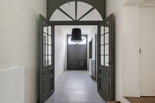 <p>Welkom in de Tweemontstraat. Van buiten zie je een statige gevel. Binnenin ontdek je 296m2 aan mogelijkheden!</p>
<p>De eerste deur die je tegenkomt? Die leidt naar een royale bureauruimte.<br />Vandaag een stijlvolle thuiswerkplek. Morgen misschien een creatieve studio of een speelkamer?<br />Nog enkele stappen verder kom je aan in de mooie, gezellige zithoek met gashaard.<br />Een zee van licht stroomt binnen via de grote ramen, en de zithoek lijkt bijna ongemerkt over te lopen in de zonnige tuin.<br />En dan zie je het. Het charmante koetshuis.<br />Een gebouw waar je automatisch naartoe wandelt. Vandaag ingericht als atelier. Maar eerlijk? Iedereen zal er iets anders in zien: een kantoor, een hobbyruimte, een plek voor logerende vrienden. Of gewoon dat ene toevluchtsoord waar je eindelijk ongestoord een boek kan uitlezen.<br />Dat is misschien wel het mooiste eraan: het geeft mogelijkheden. En mogelijkheden vervelen nooit...<br /><br />We nemen de trap naar boven en ook hier blijft de woning verrassen.<br />De keuken is geen ruimte die ergens achteraan werd weggestopt.<br />Integendeel. Ze krijgt de plaats die ze verdient. Modern, strak en afgewerkt in inox.<br />Met een royaal kookeiland waar ontbijten, aperitieven en uitgebreid koken vlot in elkaar overlopen.<br />Terwijl jij staat te koken, kijk je uit op het groene dak.<br />Aan de straatzijde ligt de eetkamer. Een ruimte waar je zonder moeite een lange tafel kwijt kan.<br /><br />Nog een verdieping hoger.<br />En hier voelt het alsof je een boetiekhotel binnenstapt.<br />De master bedroom straalt rust uit. En aansluitend is er de uitnodigende luxueuze badkamer. Een vrijstaand ligbad, een ruime inloopdouche en een dubbele lavabo.<br />Helemaal boven wachten nog twee volwaardige slaapkamers en een extra badkamer. Geen ochtendfiles aan de badkamerdeur. Dat alleen al is soms goud waard.<br /><br />Achter de charme schuilt bovendien een woning die helemaal mee is met haar tijd.<br />Met een EPC B, conforme elektriciteit, zonnepanelen, airconditioning, teleruptoren en een droge kelder zijn ook de technische fundamenten helemaal op orde. Je kan hier ook nog genieten vaan 2% registratierechten!</p>
<p>Troeven:<br />- 296 m² bew. opp.<br />- Volledig gerenoveerd<br />- EPC B<br />- AREI conform<br />- Zonnepanelen<br />- Airconditioning<br />- Mooie bureauruimte<br />- Lichtrijke leefruimte met grote glaspartijen<br />- Prachtig koetshuis met tal van mogelijkheden<br />- Moderne RVS-keuken met kookeiland<br />- Luxueuze master met ensuite badkamer<br />- Tweede badkamer<br />- Zonnige stadstuin<br />- Groendak<br />- Droge kelder<br />- Teleruptoren</p>