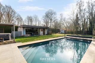 Voor meer info en foto’s, surf naar www.swevers.be – Deze open bebouwing in Zonhoven, gebouwd in 2005 en tussen 2021 en 2025 grondig geoptimaliseerd, biedt instapklaar en energiezuinig wooncomfort. De woning beschikt over een zuidgericht perceel van 12 are 33 ca met een tuin van 713,98 m², een terras van 40 m² en een verwarmd zwembad op 21 zonnepanelen.<br />Binnen geniet u van een inkomhal met gastentoilet, een lichtrijke leefruimte van 34,43 m² met gashaard en directe toegang tot het terras, en een ruime keuken van 24,99 m² uitgerust met drie ovens, een stockageruimte en aparte zij-ingang. Verder is de woning volledig onderkelderd met natuurlijke lichtinval via lichtkoepels en ingericht met kelderberging, wasplaats, bureau en een atelier/mancave van 41 m².<br />Op de verdieping vindt u vier volwaardige slaapkamers (28,35 m², 20,59 m², 16,20 m² en 11,12 m²) met ingemaakte kasten, een badkamer met ligbad, dubbele wastafel en infraroodsauna, een aparte douchekamer en apart toilet.<br />Extra troeven zijn de dubbele carport, fietsenberging, vernieuwde zwembadinstallatie, airco’s, laadpaal, vernieuwde verwarmingsketel en versterkte elektriciteit, evenals een volledig uitgerust poolhouse met eigen ingang, living, keuken, badkamer en slaapkamer – ideaal als gastenverblijf of praktijkruimte.<br />Gelegen op 450 m van scholen en openbaar vervoer, 400 m van restaurants, 2,4 km van winkels en 5,4 km van de snelweg, nabij natuurgebied De Platwijers. Voor meer informatie, bel 011 255 155. Bron bewoonbare oppervlakte: EPC – verslag.