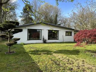 Deze gezellige woning ligt in een rustige en groene omgeving binnen het BPA Recreatief Woongebied, waar permanent wonen is toegestaan. De woning is goed onderhouden en biedt een praktische indeling met veel natuurlijk licht.<br /><br />Bij binnenkomst verwelkomt de inkomhal u met een handige vestiaireruimte en een apart toilet. Vanuit de hal loopt u zo de lichte en ruime woonkamer binnen, waar zithoek en eetplaats naadloos in elkaar overlopen. Grote ramen aan de voorzijde zorgen voor een aangename lichtinval en bieden zicht op de tuin. De ingerichte keuken grenst direct aan de eetruimte. De woning beschikt over twee comfortabele slaapkamers, ideaal voor een gezin of gasten. De badkamer is uitgerust met een moderne douche en een lavabomeubel. <br />Aan de inkomhal bereikt u het gezellig overdekte terras, perfect om te genieten van een rustige ochtendkoffie of een zomerse avond. Aan het terras bevindt zich een berging met de cv-installatie op aardgas, en achteraan het perceel staat een houten bijgebouw.<br /><br />De woning staat achteraan het perceel en is omgeven door een volledig omheinde tuin. Vooraan biedt de oprit plaats voor meerdere wagens, afsluitbaar met een poort, waardoor privacy en veiligheid gegarandeerd zijn. Beschikbaar: één maand na de notariële akte.