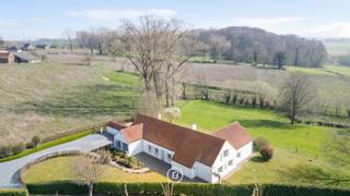 Ontdek deze charmante landelijke woning met prachtige vergezichten op een uitzonderlijk perceel van ca. 78 are, omgeven door uitgestrekte weilanden. Deze eigendom is uitermate geschikt voor kangoeroewonen of de combinatie van wonen en werken, dankzij de aparte bureauruimte en de volledig uitgeruste inpandige studio.<br /><br />Bij het betreden van de woning wordt u verwelkomd in de inkomhal met gastentoilet. De lichtrijke leefruimte vormt het hart van de woning en biedt een gezellige zithoek en eetplaats, beide met een prachtig zicht op de tuin en het omliggende landschap. Aansluitend vindt u de uitgeruste keuken met eetgedeelte, een praktische berging en een koele ruimte.<br />De woning beschikt over een polyvalente ruimte die perfect ingericht kan worden als bureau of praktijkruimte. Op het gelijkvloers bevindt zich eveneens de nachthal die toegang geeft tot de master bedroom met eigen badkamer, drie kinderkamers, een douchekamer en apart toilet.<br />Op de eerste verdieping bevindt zich de inpandige studio, voorzien van een leefruimte, keuken, slaapkamer en badkamer, ideaal voor inwonende familie. Het tweede deel van deze verdieping biedt bovendien nog tal van uitbreidingsmogelijkheden.<br /><br />De buitenomgeving is zonder twijfel een absolute meerwaarde: een zuidgericht terras en een uitgestrekte tuin met weide creëren een oase van rust en ruimte, met prachtige vergezichten over het omliggend groen.