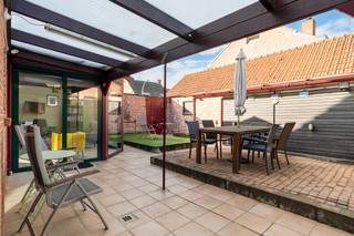 <p>Praktisch ingedeelde woning met woonkamer aansluitend op een gezellige veranda met kachel en een volledig ingerichte keuken van ca. 16m². Op het gelijkvloers bevinden zich een <strong>slaapkamer van 12,7m²</strong>, die eventueel opnieuw bij de woonkamer kan worden betrokken, een badkamer met douche, achterinkom/wasplaats en opbergveranda.</p>
<p>Op de verdieping zijn er <strong>twee ruime slaapkamers van ca. 18m² en 25m²</strong>. De grootste slaapkamer biedt door haar oppervlakte de mogelijkheid om eventueel op te splitsen in twee kinderkamers.</p>
<p>Verder beschikt de woning over een <strong>ruime garage</strong>, geschikt voor twee wagens achter elkaar of voor één wagen in combinatie met extra berg- of werkruimte. Het <strong>volledig beschutte binnenterras</strong> biedt een aangename buitenruimte waar u heerlijk uit de wind zit.</p>
<p><strong>Bijzonderheden</strong></p>
<ul>
<li><strong>3 slaapkamers</strong>, waarvan 1 op het gelijkvloers</li>
<li>Grootste slaapkamer eventueel op te splitsen</li>
<li>Gelijkvloerse slaapkamer eventueel te integreren in de woonkamer</li>
<li>Ingerichte keuken van ca. 16m²</li>
<li>Veranda met kachel</li>
<li>Achterinkom/wasplaats en extra opbergveranda</li>
<li>Ruime garage met diverse gebruiksmogelijkheden</li>
<li>Volledig beschut en windluw binnenterras</li>
</ul>