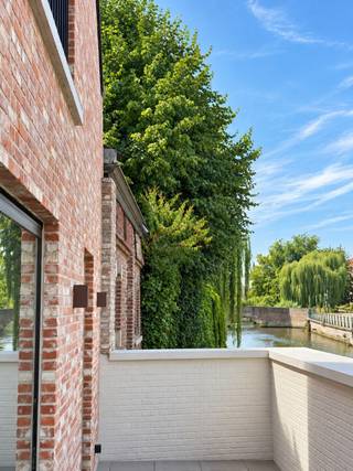 TE HUUR - GENT. Wonen in alle rust, vlak bij het hart van Gent? In het geliefde Prinsenhof vindt u deze stijlvolle nieuwbouwwoning met een prachtig uitzicht op het water. De woning is afgewerkt met kwaliteitsvolle materialen en biedt alle comfort voor wie aangenaam en zorgeloos wil wonen.<br /><br />Via het gezellige voortuintje komt u binnen in de inkomhal, waar een praktische vestiairekast en een gastentoilet voorzien zijn. De lichtrijke leefruimte voelt meteen ruim en uitnodigend aan, met een comfortabele zithoek en een royale plaats voor de eettafel. De open keuken met kookeiland is volledig ingericht en vormt het natuurlijke hart van de woning. Vanuit de leefruimte stapt u rechtstreeks het zonnige terras op. Een heerlijke plek om tot rust te komen en te genieten van het uitzicht op het water.<br /><br />Op de bovenverdieping bevinden zich drie volwaardige slaapkamers, een dressing, een afzonderlijk toilet en een moderne badkamer die stijl en comfort mooi combineert.<br /><br />Een bijzondere extra is het gemeenschappelijke binnenzwembad, waarvan de bewoners vrij gebruik kunnen maken. Zo geniet u thuis van een vleugje vakantiegevoel, het hele jaar door.<br /><br />Deze energiezuinige woning brengt rust, ruimte en hedendaags wooncomfort samen op een unieke locatie aan het water.<br /><br />De huurprijs bedraagt € 1.975 per maand, aangevuld met € 150 maandelijkse algemene kosten. Een staanplaats op het binnenplein kan worden bijgehuurd voor € 125 per maand.