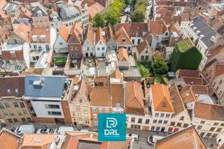 Op een <strong>absolute topligging in het historische centrum van Brugge</strong>, vlak bij het Simon Stevinplein en op wandelafstand van de Markt, bieden wij een bijzonder vastgoedensemble aan met een zelden geziene combinatie van <strong>ruimte, karakter, comfort en mogelijkheden</strong>.<br />Het geheel bestaat uit <strong>vier onroerende goederen</strong>: <strong>Zilverstraat 17</strong>, <strong>Zilverstraat 19</strong>, het woongedeelte van <strong>Steenstraat 56</strong> <em>(exclusief het handelsgelijkvloers)</em> en een <strong>overdekte staanplaats voor twee wagens in de Kopstraat</strong>.<br />De verschillende eigendommen vormen samen een uitzonderlijk geheel en bieden tal van mogelijkheden voor <strong>wonen en werken onder één dak, vrije beroepen, kantoor of praktijk, atelier, een ruime stadsresidentie of een combinatie hiervan</strong>.<br />Een absolute blikvanger is bovendien het <strong>fantastische uitzicht over de historische binnenstad, het Simon Stevinplein en de drie iconische Brugse torens</strong>.<br /><br /><u>Zilverstraat 17</u><br />Achter de brede, karaktervolle gevel gaat een verrassend ruim pand schuil.<br />Op het gelijkvloers bevinden zich een <strong>bureau-/praktijkruimte</strong>, toilet en een bijzondere multifunctionele ruimte waarin zich een <strong>binnenzwembad</strong> bevindt. Het zwembad is momenteel volledig afgedekt met een houten vloer, waardoor deze ruimte vandaag perfect als hobby- of ontspanningsruimte kan worden gebruikt. De oorspronkelijke zwembadfunctie kan opnieuw zichtbaar worden gemaakt.<br />Via de traphal bereikt men de bovenliggende woonvertrekken met onder meer een <strong>leefruimte, keuken en terras</strong>, gevolgd door een nachthal, slaapkamer en badkamer.<br /><br /><u>Zilverstraat 19</u><br />Het naastgelegen pand is onmiddellijk herkenbaar aan zijn karakteristieke <strong>vooruitstekende gevel</strong> en vormt mee de verbinding tussen de verschillende delen van het vastgoedensemble.<br />Het omvat onder meer een <strong>inkomhal, inpandige garage, kelder, toilet, twee bergingen, keuken en achterplaats</strong>.<br />Vanuit dit gedeelte is er via <strong>trap én lift</strong> verbinding met de bovenliggende verdiepingen en met Steenstraat 56.<br />De verdiepingen omvatten onder meer een <strong>bureau-/atelierruimte met toilet</strong>, meerdere kamers, verschillende badkamers, toiletten en een terrasje. Ook de zolderverdieping werd ingericht met bijkomende kamers en sanitair.<br /><br /><u>Steenstraat 56</u><br />Aan de zijde van de Steenstraat bevindt zich een bijzonder karaktervol historisch pand met een prachtige trapgevel.<br /><strong>Het handelsgelijkvloers behoort niet tot het aangeboden vastgoed.</strong><br />Het woongedeelte omvat onder meer een <strong>leefruimte, salon/zitplaats, keuken, veranda, bureau, berging en toilet</strong>. Op de verdieping bevinden zich <strong>twee slaapkamers, een badkamer en terras</strong>, aangevuld met een zolderruimte.<br />Vanuit de hoger gelegen ruimtes geniet men van prachtige vergezichten over de Brugse binnenstad en zijn monumentale skyline.<br /><br />Ondanks het uitgesproken historische karakter beschikt het geheel over verschillende hedendaagse comfortelementen. Zo zijn er <strong>diverse airconditioningstoestellen</strong> aanwezig en zorgt de <strong>lift</strong> voor extra comfort en een praktische verbinding tussen verschillende niveaus van het complex. De combinatie met het binnenzwembad, terrassen en buitenruimtes maakt het geheel des te uitzonderlijker.<br /><br />Een niet te onderschatten troef in het centrum van Brugge is de aanwezigheid van een <strong>overdekte staanplaats voor twee wagens in de Kopstraat</strong>. Samen met de garage in Zilverstraat 19 betekent dit een bijzonder waardevolle parkeerfaciliteit op een locatie waar private parkeermogelijkheden uiterst schaars zijn.<br /><br />Dit is geen klassieke stadswoning, maar een <strong>uniek en veelzijdig vastgoedensemble</strong> met verschillende adressen en toegangen, royale volumes, garage, lift, zwembad, terrassen, werk- en praktijkruimtes en parkeerplaats voor twee wagens.<br /><br />Meer info of een bezoek inplannen, bel of mail DRL VASTGOED, 050 65 95 95 of info@drlvastgoed.be<br />