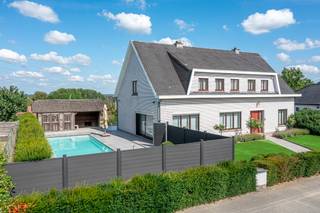 <p>Deze ruime villa uit 1980 biedt een mooie combinatie van wonen, ontspanning en tal van extra mogelijkheden. Aan de voorzijde beschikt de woning over een mooie voortuin. Links naast de woning bevindt zich het zwembad met aansluitend een ruim terras en poolhouse met douche. Achter de woning is er bovendien een groot terras.</p><p>Op het gelijkvloers beschikt de woning over een ruime inkomhal, aparte bureauruimte, toilet, ingerichte keuken met bijkeuken en aansluitende berging, een eetplaats in een ruime L-vormige leefruimte. Dankzij het grote schuifraam staat de leefruimte rechtstreeks in verbinding met het terras en de buitenruimte.</p><p></p><p>De eerste verdieping omvat een nachthal, badkamer met ligbad, douche en dubbele wastafel en vijf ruime kamers. Deze kunnen naar eigen behoefte worden ingericht als slaapkamers, bureau, hobbyruimte of fitnessruimte.</p><p><strong>Een absolute troef is de grote loods onder de woning.</strong> Deze beschikt over drie hoge inrijpoorten, een interne laadkade en frigo- en koelinstallaties. De loods biedt heel wat mogelijkheden voor een zelfstandige activiteit, opslag, werkplaats of hobby. Ook voor liefhebbers van oldtimers, verzamelaars of wie meerdere voertuigen wil stallen, is dit een bijzonder interessante ruimte.</p><p></p><p>De loods is bereikbaar via de oprit rechts van de woning via de Oude Geraardsbergsebaan, <strong>Daarnaast is er een tweede, vlottere toegang tot de loods rechtstreeks vanaf de Ninoofsesteenweg</strong>, via het afzonderlijke perceel bouwgrond. Dit perceel, inclusief deze toegang, kan apart worden aangekocht. Hierdoor beschikt de loods over een bijzonder praktische ontsluiting, ook voor grotere voertuigen of vrachtwagens. Dit maakt het geheel onder meer interessant voor een zelfstandige activiteit, opslag, een werkplaats of het stallen van voertuigen en oldtimers.</p><p></p><p>Een veelzijdig eigendom voor wie op zoek is naar een ruime woning en grote buitenruimte, gecombineerd met een uitzonderlijke loods en tal van mogelijkheden.</p><p></p><p><strong>EPC: label C – 266 kWh/m²/jaar</strong></p>