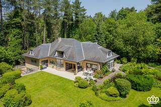 <p><span>Residentieel gelegen villa op een privacyrijk perceel van 2.672 m², tegenover een natuurgebied en nabij het centrum van Heide-Kalmthout, met o.a. een ruime en lichtrijke leefruimte, leefkeuken, vijf royale slaapkamers, drie ingerichte badkamers en een wellnessruimte met binnenzwembad en sauna.  </span></p><p><span>Gelijkvloers</span></p><p><span>U betreedt de woning via een ruime inkomhal op natuurstenen vloer, voorzien van een gastentoilet met handenwasser en een vestiaire. Deze hal geeft toegang tot de royale en lichtrijke leefruimte op parketvloer, onderverdeeld in een tv-hoek, een zithoek met erker en gashaard en een eetruimte.</span></p><p><span>Aansluitend bevindt zich de volledig uitgeruste leefkeuken met alle hedendaagse toestellen, waaronder een combi-oven, microgolf, inductievuur met ingebouwde dampkap, spoelbak met Quooker-kraan, een grote koelkast, een vriezer en een vaatwasser. De ontbijthoek biedt directe toegang tot het overdekte terras met uitzicht op de prachtig aangelegde tuin.</span></p><p><span>Daarnaast beschikt het gelijkvloers over een masterbedroom op laminaatvloer met aansluitend een dressing en een ingerichte badkamer. Deze is uitgerust met een inloopdouche voorzien van een infrarood Sunshower, een ligbad, dubbele wastafel, toilet en handdoekenradiator.</span></p><p><span>Ten slotte is er nog een dubbele inpandige garage met automatische poort, waar zich eveneens de aansluitingen voor wasmachine en droogkast bevinden.</span></p><p><span> </span></p><p><span>Eerste</span><span> </span><span>verdieping</span></p><p><span>Via de royale trap met vide bereikt u de nachthal, waar zich een apart toilet en een bergkast bevinden. Bovendien heeft u toegang tot een knus balkon. Op deze verdieping bevinden zich vier zeer ruime slaapkamers en een tweede badkamer, ingericht met een douche, ligbad, wastafel, toilet en handdoekenradiator.</span></p><p><span> </span></p><p><span>Zolder</span></p><p><span>Via een vlizotrap heeft u toegang tot de bergzolder.</span></p><p><span> </span></p><p><span>Kelder</span></p><p><span>Middels de centrale trappartij bereikt u de kelder, opgedeeld in drie compartimenten: een bergruimte, een technische ruimte en een ontspanningsruimte. Deze laatste is uitgerust met een zwembad (4 m x 9 m) met jetstream, een traditionele sauna en een badkamer voorzien van een douche, wastafel en toilet. Via een schuifdeur heeft u toegang tot een aangenaam omsloten terras.</span></p><p><span> </span></p><p><span>Tuin</span></p><p><span>De woning is gelegen op een volledig omheind perceel van ca. 2.650 m². De prachtig aangelegde tuin die volledige privacy biedt en veel zoninval geniet, is voorzien van een irrigatiesysteem en meerdere vijverpartijen, die bijdragen aan een rustgevende en groene leefomgeving.</span></p><p><span>Bijzonderheden</span><span><br />-Charmante villa in klassieke/tijdloze stijl <br />-Recent gemoderniseerd o.a. keuken, badkamers, vloeren, …. <br />-Verrassend ruim<br />-Volledige privacy <br />-Fraai aangelegde en goed onderhouden tuin met veel zoninval<br />-Zuid-west georiënteerd<br />-Goed beveiligd<br />-Binnenzwembad en sauna in de kelder met buitenterras<br />-Rustig in het groen gelegen, tegenover natuurgebied en nabij dorpscentrum (scholen, winkels en  openbaar vervoer). <br />-Elektrische keuring is conform.<br />-Geen asbest</span></p><p><span> </span></p>