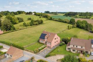 Deze indrukwekkende en perfect onderhouden woning combineert ruimte, comfort en een uitzonderlijke ligging op een prachtig perceel met weids groen uitzicht. Dankzij de royale oppervlaktes, kwalitatieve afwerking en doordachte indeling is dit een ideale gezinswoning met tal van mogelijkheden.<br />Bij het betreden van de woning komt u terecht in een ruime en statige inkomhal met gastentoilet. De lichtrijke woon- en eetkamer beschikt over een royale zithoek rond de sfeervolle open haard, voorzien van een praktische lift naar de kelder waar de houtvoorraad zich bevindt. Aansluitend bevindt zich de volledig vernieuwde keuken met bijkeuken en toegang tot de kelder.<br />Het gelijkvloers beschikt bovendien over een ruime slaapkamer en een badkamer, wat de woning bijzonder geschikt maakt voor gelijkvloers wonen, minder mobiele bewoners of levenslang wonen.<br />De woning is volledig onderkelderd en omvat onder meer een uitzonderlijk ruime inpandige garage met plaats voor vier wagens, een werkruimte, technische ruimte en extra opslagmogelijkheden.<br />Op de eerste verdieping bevinden zich drie zeer ruime slaapkamers. De master bedroom beschikt over twee dressings, waarvan één de oppervlakte heeft van een volwaardige extra slaapkamer. Verder zijn er twee badkamers en een apart toilet aanwezig.<br />Via de ruime nachthal bereikt u de tweede verdieping, die in 2025 werd ingericht en plaats biedt aan nog twee slaapkamers en een vierde badkamer.<br />Ook op vlak van energiezuinigheid scoort deze woning uitstekend dankzij de aanwezigheid van zonnepanelen en een warmtepompboiler. De keuken, badkamers en parketvloeren werden bovendien kwalitatief gerenoveerd, waardoor de woning zich in absolute topconditie bevindt.<br />De achtertuin vormt zonder twijfel één van de grootste troeven van deze eigendom: een gigantisch grasveld met een uniek en rustgevend uitzicht op het omliggende groen.<br />Een uitzonderlijke woning voor wie op zoek is naar ruimte, comfort, kwaliteit en een unieke woonomgeving.<br />Beschikbaar vanaf 01/07/2027.