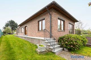 Bent u op zoek naar een bungalow die ruimte, comfort en uitzonderlijke mogelijkheden combineert voor zowel wonen als werken? Dan zal deze solide halfopen bebouwing uit 1994 u meteen weten te overtuigen. Met haar doordachte indeling, overvloed aan opslagruimte en prachtige tuin is dit de ideale thuisbasis voor gezinnen én zelfstandigen of thuiswerkers.<br /><br />Een van de grootste troeven van deze woning is zonder twijfel de volledig onderkelderde verdieping van maar liefst circa 130 m². Deze biedt plaats aan meerdere wagens, maar leent zich evengoed perfect als opslagruimte, atelier, hobbyruimte of professionele werkplek. Dankzij de toegang via een garagepoort én een deur naar de tuin is deze ruimte uiterst praktisch en veelzijdig in gebruik.<br /><br />Op het gelijkvloers wordt u verwelkomd in een karaktervolle inkomhal met trap, die meteen de degelijkheid van de woning weerspiegelt. Verder vindt u hier een gastentoilet, een handige berging of dressingruimte, een badkamer met ligbad en douche en twee ruime slaapkamers. Deze indeling maakt de woning bovendien bijzonder geschikt voor wie levenslang comfortabel wil blijven wonen.<br /><br />De lichtrijke leefruimte met open keuken van 64 m² vormt het hart van de woning en nodigt uit tot gezellige momenten met familie en vrienden. Grote raampartijen zorgen voor een aangename lichtinval en bieden een mooi zicht op de tuin. De open haard voegt extra warmte en sfeer toe, terwijl de volledig geïnstalleerde keuken voorzien is van alle nodige toestellen.<br /><br />Onder het dak bevindt zich een extra kamer van 37 m² die eenvoudig kan worden opgedeeld in meerdere slaapkamers, een bureau of hobbyruimte, afhankelijk van uw noden. Dit biedt tal van uitbreidingsmogelijkheden voor grotere gezinnen of wie extra werkruimte wenst.<br /><br />EPC D – 315 kWh / Dubbel Glas / Centrale verwarming / Regenwaterput – 10.000 L / Kelder 130 m² / Woonruimte 181 m² / Betonstructuur / … Op te frissen.<br /><br />De woning is gelegen op een ruim perceel van net geen 18 are. Hier heeft u alle ruimte om kinderen vrij te laten spelen, een moestuin aan te leggen of dieren te houden.<br /><br />Ook de ligging is een absolute troef met scholen, winkels, openbaar vervoer en belangrijke verbindingswegen zoals de E40 op korte afstand. Daarnaast biedt de omgeving tal van mogelijkheden voor wandelen, fietsen en ontspannen in het groen.<br /><br />Bent u op zoek naar een veelzijdige woning met ruimte in overvloed en tal van mogelijkheden voor wonen en werken? Contacteer ons vandaag nog en plan uw bezoek!