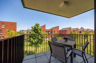 <p><span>Geen zin in verbouwen, schilderen of verrassingen? Dan zit je hier goed. Dit appartement uit 2017 ligt in een jonge woonwijk waar kinderen nog op straat spelen en buren elkaar kennen. Je woont hier rustig, met een supermarkt om de hoek, het Boekenbergpark vlakbij en een Velostation letterlijk voor de deur.</span></p><p><span> </span></p><p><span>Binnenkomen en je jas neergooien</span></p><p><span>De inkomhal is slim ingedeeld voor een vestiaire. Verderop opent het appartement zich meteen naar de leefruimte. Geen verloren vierkante meters hier, maar een logische indeling waarbij koken, eten en ontspannen mooi in elkaar overvloeien.</span></p><p><span>De woonkamer krijgt langs verschillende kanten daglicht binnen dankzij de hoekligging. Terwijl je aan tafel zit, kijk je uit op het groen en de jonge wijk rondom je. Geen gevel op twee meter afstand, maar een open gevoel dat je in veel appartementen mist.</span></p><p><span>De keuken houdt het strak en eenvoudig, met witte greeploze kasten, een inductiekookplaat, combi-oven, vaatwasser en flink wat opbergruimte. Achteraf verdwijnen de boodschappen gewoon in de aansluitende berging, zodat het werkblad netjes blijft.</span></p><p><span> </span></p><p><span>Koffie buiten, zelfs als het regent</span></p><p><span>Op het overdekte terras zit je beschut en toch buiten. Groot genoeg voor een tafeltje en enkele stoelen. Dankzij het vele groen in de omgeving voelt het hier verrassend rustig aan voor een locatie zo dicht bij de stad.</span></p><p><span>Verder zijn er twee slaapkamers. De grootste biedt voldoende plaats voor een dubbel bed en een ruime kast. De tweede kamer doet even vlot dienst als kinderkamer, bureau of dressing.</span></p><p><span>De badkamer kreeg een verzorgde, tijdloze afwerking met een ruime inloopdouche en een dubbel lavabomeubel. Geen ochtenddiscussies meer over wie eerst aan de wastafel staat.</span></p><p><span> </span></p><p><span>Praktisch wonen</span></p><p><span>Ook aan de minder zichtbare zaken werd gedacht. Er is een aparte plek voor wasmachine en droogkast, een ruime kelderberging voor spullen die je niet dagelijks gebruikt en een ondergrondse parkeerplaats die verplicht mee aan te kopen is. Thuiskomen en niet meer rondjes rijden op zoek naar een vrije plek: het lijkt een detail, tot je het gewoon bent.</span></p><p><span> </span></p><p><span>Jong, groen en verrassend goed verbonden</span></p><p><span>Deze buurt trekt vooral jonge gezinnen en starters aan. Kinderen spelen in de buurt, de speeltuin ligt vlakbij en voor een wandeling hoef je niet verder dan het Boekenbergpark. Met tram, bus, velo en de Ring vlakbij geraak je bovendien snel waar je moet zijn, zonder midden in de drukte te wonen.</span></p><p><span><br />maatregelregister in aanvraag </span></p>