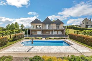 <p>Voor meer info of een bezoek, bel 054 69 39 37 – Deze <strong>indrukwekkende villa </strong>combineert elegante architectuur met een uitzonderlijke ligging nabij alle voorzieningen. Met een bruikbare vloeroppervlakte van 747 m² biedt deze eigendom alles voor wie op zoek is naar luxe, ruimte en comfort op een <strong>absolute toplocatie</strong>.</p>
<p>Bij het betreden van de woning wordt u verwelkomd in een royale inkomhal met praktische dressing. De lichtrijke woonkamer, dankzij de grote raampartijen, biedt een prachtig zicht op de <strong>perfect onderhouden tuin</strong>. In de wintermaanden zorgt de open haard voor extra sfeer en gezelligheid. Aansluitend bevindt zich de elegante eetkamer, ideaal voor gezellige diners en het ontvangen van gasten.</p>
<p>De volledig uitgeruste keuken sluit naadloos aan op het ruime <strong>zonneterras</strong>, vanwaar u een adembenemend uitzicht heeft op het <strong>zwembad </strong>en het achterliggende groen. Hier geniet u dagelijks van rust en privacy.</p>
<p>De villa beschikt over meerdere ruime slaapkamers, waarbij de master bedroom is voorzien van een <strong>eigen luxe badkamer en ruime dressing</strong>. Op de verdieping vindt u bovendien een grote zitruimte met mezzanine, een polyvalente opslagruimte en een ruime, gemakkelijk toegankelijke zolderkamer.</p>
<p>Als extra troef is de woning <strong>volledig onderkelderd</strong>. Hier bevindt zich een zeer ruime garage met plaats voor maar liefst<strong> 6 à 7 wagens</strong>, een praktische kitchenette, een douchecabine en verschillende opslagmogelijkheden. Deze ruimte biedt tal van mogelijkheden voor hobby's, opslag of extra comfort.</p>