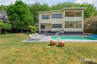 Karaktervolle Art-Deco villa met potentieel op toplocatie<br />In een geliefde en goed bereikbare omgeving vindt u deze ruime villa in authentieke Art-Deco stijl (vroeger dokterswoning) Dankzij de royale ruimtes en veelzijdige indeling biedt deze woning tal van mogelijkheden voor wie op zoek is naar comfort én karakter.<br />De entree maakt meteen indruk: een ronde inkomhal met vide, waar het daglicht via een dakraam prachtig naar binnen valt. Vanuit deze hal bereikt u een riante woonkamer die naadloos aansluit op een gezellige tv-kamer. Verder zijn er een afzonderlijk bureel, een aparte eetkamer met toegang tot het overdekte terras én een volledig ingerichte keuken die eveneens rechtstreeks vanuit de eetkamer toegankelijk is.<br />Op de bovenverdieping verbindt een gaanderij, die rond de vide loopt, alle kamers met elkaar. Er is een logeerkamer met dakterras, twee ruime slaapkamers en een badkamer. De master suite beschikt over een dressing, een privébadkamer en een slaapkamer met toegang tot een tweede overdekt terras.<br />De villa is nagenoeg volledig onderkelderd, wat extra ruimte oplevert voor opslag, een garage, hobbyruimte en technische voorzieningen.<br />Naast het dakterras en de twee overdekte terrassen vindt u meerdere zonneterrassen rond het verwarmde zwembad. De omheinde tuin garandeert volledige privacy en een rustige setting.<br />De woning is goed onderhouden en uitgerust met hedendaags comfort. Met enkele gerichte verbeteringen kan dit pand uitgroeien tot een werkelijk uniek eigendom binnen zijn klasse.<br />EPC C, G en P score : A,