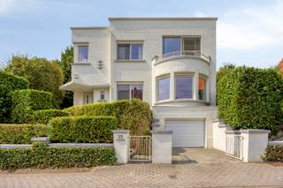 <p>Op een bijzonder fijne locatie in een aangename woonwijk, vlakbij het centrum van Dilbeek, bevindt zich deze karaktervolle architectenwoning uit het interbellum. De woning is een mooi voorbeeld van de architectuur uit die periode, waarin invloeden van art deco, traditionalisme en strak modernisme samenkomen. Opvallende volumes, ambachtelijk metselwerk, geometrische vormen en grote raampartijen geven de woning haar uitgesproken karakter en zorgen bovendien voor een overvloed aan natuurlijk licht. Heel wat authentieke elementen bleven mooi bewaard en worden vandaag gecombineerd met hedendaags wooncomfort.</p><p> </p><p>Achter de charmante gevel wordt u verwelkomd in een mooie inkomhal die meteen de authentieke sfeer en architecturale eigenheid van de woning weerspiegelt. Een apart toilet en een ruime centrale hal leiden naar de verschillende leefruimtes.</p><p>De royale leefruimte is een absolute blikvanger, met een prachtige parketvloer, veel natuurlijk licht en een warme uitstraling. Aansluitend bevindt zich de keuken met gezellige eethoek. Daarnaast beschikt de woning over een aparte bureauruimte en een vestiaire-/multifunctionele ruimte die naar eigen behoefte kan worden ingericht.</p><p>Vanuit de leefruimtes is er toegang tot het mooie terras en de heerlijke tuin. Een groene oase met veel privacy en verschillende gezellige hoekjes waar u op elk moment van de dag een aangename plek vindt om te ontspannen, te genieten of gasten te ontvangen.</p><p> </p><p>Op de eerste verdieping bevinden zich vier slaapkamers en een badkamer met zowel een douche als een ligbad. De hoofdslaapkamer heeft als extra troef een rechtstreekse toegang tot een groot terras, terwijl ook de slaapkamer aan de voorzijde toegang biedt tot een balkon.</p><p>De zolderverdieping biedt nog bijkomend potentieel en kan naar eigen wensen worden ingericht: een hobbyruimte, speelruimte of atelier behoren tot de mogelijkheden.</p><p>De woning is grotendeels onderkelderd en beschikt bovendien over een grote garage, wat zorgt voor praktische bergruimte.</p><p> </p><p>Ook energetisch werd de woning recent grondig aangepakt. Zo werden onder meer nieuwe ramen geplaatst, 18 zonnepanelen met batterij geïnstalleerd, het dak vernieuwd en geïsoleerd en een nieuwe gasketel geplaatst. Zo blijft het uitgesproken interbellumkarakter behouden, terwijl de woning tegelijk geniet van hedendaags comfort en een verbeterde energie-efficiëntie.</p><p>De authentieke architectuur vormt hier duidelijk de basis. Tegelijk biedt de woning ruimte om bepaalde vertrekken naar eigen smaak verder te verfijnen en te actualiseren. </p><p> </p><p>De ligging is bijzonder praktisch: op wandelafstand van het centrum van Dilbeek via fiets- en voetgangerstunnel en van winkels, scholen en openbaar vervoer. Tegelijk geniet u van de rust en het aangename karakter van een fijne woonwijk.</p><p>Een bijzondere architectenwoning met een uitgesproken interbellumkarakter, royale ruimtes en een prachtige parktuin. Een unieke combinatie van architecturale eigenheid, authenticiteit, ruimte en hedendaags wooncomfort, op een gegeerde locatie in Dilbeek.</p>