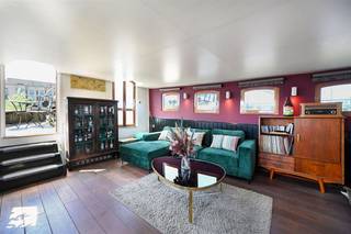 Bekijk deze boot uitgebreid op www.koosi.beDeze prachtige woonboot ‘Ons Genoegen’ is een blikken klipper van 1893 die ooit gebouwd is om steenkool te vervoeren over het water. De boot is gelegen op de mooiste plaats aan het Houtdok-Zuidkaai, de instapprijs van de concessie is inbegrepen in de koopsom. De romp is gemaakt uit staal van 6 mm dik en is de laatste keer officieel gecontroleerd in oktober 2024. Via de aanlegsteiger betreden we de boot en komen we op het achterdek waar de stuurinrichting van de boot is geplaatst. Als we dan binnenkomen in de leefruimte voelen we direct de gezelligheid die deze woonboot kan bieden, zeker door de aanwezigheid van de speksteenkachel. Deze ruimte is zeer groot en door de leuke lichtinval wordt dit nog eens extra benadrukt. Op het hogere deel is momenteel het salon geplaatst vanwaar je door de vele ramen direct zicht hebt op het water. Als we dan een paar trappen naar beneden lopen komen we in het gedeelte waarin de zeer ruime en volledig ingerichte keuken is gebouwd. Aan de andere kant vinden we de grote eettafel en toegang tot de ‘kelderruimte’. In voorste deel van boot zijn de slaapvertrekken voorzien. Vanuit de leefruimte komen we in een gang met rechts een berging waar wasmachine en droogkast kunnen geplaatst worden. Aan de overzijde van deze berging vinden we de technische ruimte met verwarmingsketel en pompen. Naast deze technische ruimte is het toilet gelegen. Iets verder in de gang vinden we rechts (stuurboordzijde) een slaapkamer met dubbel bed. Over deze slaapkamer (bakboordzijde) is de eerste badkamer met douche voorzien. Nog iets verder rechts is dan de 2de slaapkamer voorzien, deze kamer is momenteel ingericht als dressing en heeft een enkel bed. Over deze slaapkamer ligt de 2de badkamer, ook voorzien met lavabo en douche. Helemaal vooraan de boot komen we in de grote slaapkamer met ingebouwde kasten.