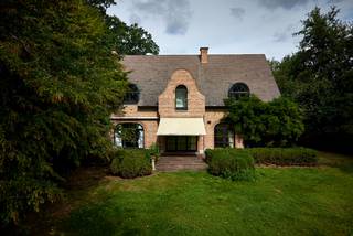 Op een bijzonder mooie en rustige locatie in het residentiële Schotenhof bevindt zich deze karaktervolle familievilla, omgeven door een volwassen tuin en genietend van een uitzonderlijke privacy.<br /><br />De eigendom combineert een royaal woonvolume met een warme, tijdloze uitstraling en een sterke verbondenheid met de tuin. Dankzij de uitstekende zuidoriëntatie, de verschillende leefruimtes en het charmante eiken bijgebouw is dit bovenal een huis waar binnen- en buitenleven op een vanzelfsprekende manier in elkaar overvloeien.<br /><br />Ook de ligging is bijzonder aangenaam: discreet en groen, maar tegelijk op korte afstand van zowel Schoten als ’s-Gravenwezel, met scholen, winkels en gerenommeerde sportclubs in de onmiddellijke omgeving.<br /><br />Een huis met ruimte en karakter<br /><br />De woning wordt benaderd via een royale voortuin met sfeervolle waterpartij. Enkele treden leiden naar de brede inkomdeur en de ruime ontvangsthal, van waaruit dubbele glazen deuren meteen een mooie doorkijk bieden naar de leefvertrekken en het groen rondom.<br /><br />De natuurstenen vloer loopt harmonieus door naar de verschillende leefruimtes. Het iets hoger gelegen salon met open haard vormt een intieme en sfeervolle plek, terwijl het aansluitende eetgedeelte zich naar de tuin richt. Grote raampartijen aan zowel voor- als achterzijde zorgen doorheen de woning voor veel natuurlijk licht en een voortdurend contact met de omgeving.<br /><br />Centraal in het dagelijkse leven staat de ruime leefkeuken. De karaktervolle AGA vormt er het hart van de ruimte, aangevuld met Miele-inbouwapparatuur en een royaal eiland waaraan ook informeel kan worden gegeten. Een glazen deur opent rechtstreeks naar het terras en de zuidgerichte tuin.<br /><br />Aansluitend bevindt zich een afzonderlijke kamer die zich uitstekend leent als bureau, bibliotheek of polyvalente ruimte en eveneens toegang biedt tot het terras. Een ruime bijkeuken zorgt voor het nodige praktische comfort.<br /><br />De dubbele inpandige garage biedt plaats aan twee wagens en beschikt over bijkomende bergruimte.<br /><br />Privévertrekken<br /><br />Op de eerste verdieping bevinden zich de hoofdslaapkamer en drie bijkomende slaapkamers, samen met twee badkamers. Talrijke ingemaakte kasten zorgen voor een bijzonder praktische indeling.<br /><br />Een afzonderlijke trap leidt verder naar een verrassend royale bovenverdieping met mezzanine. Een ruimte die zich naar eigen behoefte laat invullen als bijkomende slaapkamer, gastenverblijf, hobbyruimte of thuisbureau. Ook de zolder is vanaf hier bereikbaar.<br /><br />De woning beschikt bovendien over een zeer ruime kelderverdieping, waardoor ook aan berging en technische ruimte geen gebrek is.<br /><br />Een tuin in alle privacy<br /><br />De volwassen tuin vormt een essentieel onderdeel van de beleving van deze eigendom. De zuidelijke oriëntatie, het vele groen en de afwezigheid van inkijk creëren een bijzonder aangename en besloten sfeer.<br /><br />Een mooi uitgevoerd eiken bijgebouw, voorzien van verwarming en bergruimte, geeft de tuin nog een extra dimensie en biedt mogelijkheden voor wie op zoek is naar een afzonderlijke werk-, hobby- of ontspanningsruimte.<br /><br />Een eigendom die niet zozeer overtuigt door één afzonderlijk element, maar door het geheel: ruimte, privacy, groen en een bijzonder aangename woonkwaliteit op één van de meest gegeerde residentiële locaties van Schoten.<br /><br />Bijzonderheden<br /><br />• Residentieel en discreet gelegen in Schotenhof<br />• Op korte afstand van Schoten en ’s-Gravenwezel<br />• Royale familievilla met vijf mogelijke slaapkamers<br />• Twee badkamers<br />• Ruime leefkeuken met AGA<br />• Zuidgerichte tuin met uitzonderlijke privacy<br />• Verwarmd eiken bijgebouw<br />• Dubbele inpandige garage en bijkomende garage<br />• Royale kelder- en bergruimtes<br />• Nabij scholen, winkels en gerenommeerde sportfaciliteiten