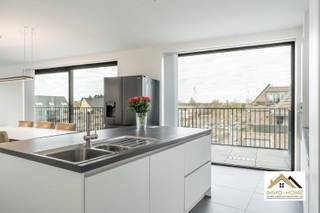 Vanuit dit prachtige penthouse bent u vanaf dag 1 ook de eigenaar van de volledige skyline van Wachtebeke-centrum. De bijzonder lichtrijke leefruimte met open keuken baadt in het daglicht door de grote raampartijen en zo ziet u vanuit elke hoek het dagelijkse leven in het dorp als een continue bewegend schilderij voorbij glijden - zonder er evenwel enige last van te ondervinden. De keuken is voorzien van alle moderne comfort, vanachter het ruime kookeiland is er eveneens altijd een bijzonder uitzicht. Net naast de keuken is er een grote opslagruimte/wasplaats aanwezig. Een lange gang (rechtstreeks bereikbaar met de lift en uiteraard ook via de trap) brengt je tot in de twee slaapkamers, waarvan de grootste is voorzien van een mooie dressing. De badkamer beschikt over een riante inloopdouche, en in de gang is er een apart toilet aanwezig. Van het buitenleven genieten doe je op het grote zonovergoten terras, dat via de schuifdeuren van de leefruimte bereikbaar is. Er is verplicht een garage aan te kopen voor €25 000 en een parkeerplaats in het gebouw inbegrepen de prijs. Nog 3 jaar vrijgesteld van OV. Inschrijvingen via mail naar tommy@immo-home.be, geen telefonische inschrijvingen! Volg ons op Fb en insta. Voor meer info: www.immo-home.be GRATIS SCHATTING GRATIS FINANCIEEL ADVIES