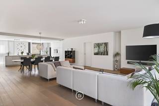 Achter de gevel van Residentie Mondriaan schuilt een bijzonder ruim appartement waar de buitenruimte meteen de toon zet. Een royaal, zuidgericht dakterras van 100 m², groen aangelegd met niet-woekerende bamboe, olijfbomen en lavendel, met charmant open zicht op de kerktoren.<br /><br />Gelegen in een kleinschalige residentie beschikt het appartement over een bruto bewoonbare oppervlakte van circa 185 m² en is volledig instapklaar. De voorgevel verwijst subtiel naar het werk van kunstschilder Piet Mondriaan en geeft het gebouw een herkenbare signatuur.<br /><br />Bij aankomst brengt de privétoegang via de lift u rechtstreeks in het appartement. Ingebouwd kastwerk bij de lift zorgt voor een verzorgde en praktische ontvangst. Van daaruit opent het geheel zich naar een ruime leefruimte, waar licht, volume en rust samenkomen.<br /><br />De doorlopende eiken parketvloer, het witte maatwerk en de kwaliteitsdeuren zorgen voor een rustig interieur. Brede raampartijen met hoogrendementsglas brengen het daglicht rijkelijk binnen en versterken het ruimtelijke gevoel. Eetruimte, salon en bureauruimte vormen samen één open leefomgeving, met het royale terras als natuurlijk verlengstuk. In de leefruimte is bovendien de mogelijkheid voorzien om een gashaard aan te sluiten. <br /><br />De keuken sluit volledig aan op de leefruimte en is strak opgevat met wandkasten, een kookeiland met een werkblad van maar liefst 5 m, ingewerkte lades en ingebouwde toestellen van onder meer Smeg en Siemens. <br /><br />Het terras vormt de uitgesproken meerwaarde van dit appartement. Door de oppervlakte, de zuidgerichte oriëntatie en de groenaanleg ontstaat een buitenruimte die verder gaat dan een klassiek terras. De antislip terrastegels, lavendel, niet-woekerende bamboe, olijfbomen, stroomaansluitingen en automatische bewatering maken deze plek geschikt voor dagelijks gebruik, lange avonden buiten en genieten van alle rust en gezelligheid. <br /><br />Het slaapgedeelte is apart ingedeeld. Beide slaapkamers beschikken over een eigen badkamer met wastafelmeubel en inloopdouche. De master heeft daarnaast een ligbad, ingebouwde maatkasten en toegang tot een afzonderlijk balkon. Beide slaapkamers zijn voorzien van extra comfort, waaronder airco of warmtebron en tv-aansluiting. Ook aan praktische details werd gedacht, zoals vliegenramen.<br /><br />Technisch is het appartement optimaal en zorgvuldig uitgerust met automatische screens, ventilatie type C die zich automatisch aanpast, brandalarm, jaarlijks gecontroleerde brandbeveiliging, een Viessmann-gasketel en een berging met aansluitingen voor wasmachine en droogkast.<br /><br />Verder beschikt het appartement over EPC-label A met een energiescore van 84 kWh/m² jaar. <br /><br />Ondergronds is een privatieve staanplaats inbegrepen.<br /><br />Een bijzonder ruim en energiezuinig appartement met een royale private buitenruimte die de woonbeleving hier op een uitzonderlijke manier versterkt.