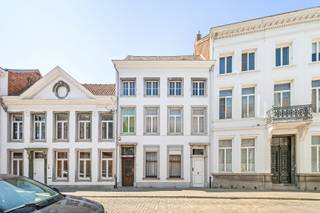 Achter deze statige gevel schuilt een uitzonderlijke herenwoning met een bewoonbare oppervlakte van maar liefst 546 m². Authentieke elementen werden doorheen de woning met zorg bewaard en versterken het unieke karakter van deze eigendom. De royale volumes, dubbele toegang en flexibele indeling maken deze eigendom uitermate geschikt voor wie op zoek is naar een ruime gezinswoning, een combinatie van wonen en werken of een eigendom met uiteenlopende gebruiksmogelijkheden.<br /><br />De woning maakt deel uit van het beschermde stadsgezicht ‘Vredeberg’ en is opgenomen als bouwkundig erfgoed. Hierdoor is de residentiële renovatieverplichting niet van toepassing.<br /><br />Via de centrale inkomhal bereikt u de bureau- of praktijkruimte, de ruime eetkamer en de lichtrijke leefruimte met een prachtig groen zicht op de privatieve tuin van 185m². De afzonderlijke keuken biedt alle ruimte en comfort voor dagelijks gebruik. Op het gelijkvloers bevinden zich verder een slaapkamer of polyvalente ruimte met ingemaakte kasten, een gastentoilet, berging, wasruimte, toegang tot de droge kelder en een bijkomende binnenplaats van 25m².<br /><br />De onderhoudsvriendelijke mediterrane tuin vormt een rustige buitenruimte en geeft rechtstreeks toegang tot de dubbele garage met elektrische poort en extra opbergruimte, bereikbaar via het Vlietje.<br /> <br />De eerste verdieping is bereikbaar via de statige trappenhal of comfortabel met de lift, die eveneens toegankelijk is via de tweede inkomdeur. Hier bevinden zich vier volwaardige slaapkamers, waarvan één met een ensuite badkamer voorzien van douche, bidet en dubbel lavabomeubel. Daarnaast is er een tweede badkamer met ligbad, toilet en lavabomeubel.<br /> <br />Een absolute troef is de voormalige tandartspraktijk op de tweede verdieping. Met een oppervlakte van maar liefst 177 m² biedt deze verdieping uitzonderlijk veel potentieel voor extra woonruimte, een praktijk, atelier of een andere invulling. Aansluitend bevinden zich nog twee ruime zolderverdiepingen, die bijkomende mogelijkheden bieden.