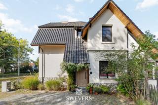Voor meer info en foto’s, surf naar www.swevers.be – In de Koolmijnlaan 285 te Heusden-Zolder ontdek je deze charmante halfopen woning met rijke geschiedenis, gebouwd in 1924. De gevel met cederhouten accenten en acaciahouten voordeur straalt warmte uit, terwijl tal van vernieuwingen zorgen voor hedendaags comfort. Zo werd het dak vernieuwd in 2008, de gevel en ramen aangepakt in 2019 en kreeg de verwarmingsketel in 2024 nog een nieuwe brander. Binnen geniet je van een gezellige leefruimte met authentieke elementen zoals houten vloeren en sierlijsten. De keuken van 13 m² met veranda biedt veel licht en een prachtig zicht op de tuin. Verder zijn er een badkamer, wasplaats en inpandige garage van 17,66 m² aanwezig. Het perceel van 4a 88ca is volledig omheind, mooi aangeplant en geniet van een noordoostelijke oriëntatie met privacy en ochtendzon. Boven zijn er drie slaapkamers (13,38 m² – 13,83 m² – 7,65 m²) en een ruime zolder van 35,17 m² met uitbreidingsmogelijkheden. Extra troeven zijn de droge kelder van 11,85 m² en de vlotte bereikbaarheid dankzij de nabijheid van winkels, scholen en de E314. Deze woning combineert charme, authenticiteit en een zonnige tuin in een bruisende buurt – ideaal voor gezinnen die op zoek zijn naar karakter en comfort. Voor meer informatie, bel 011 255 155. Bron bewoonbare oppervlakte: EPC – verslag.