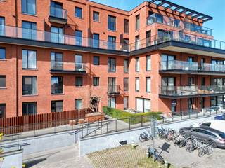 Dit lichtrijk gelijkvloers appartement maakt deel uit van de succesvolle ontwikkeling <em>København</em>. Deze residentie bevindt zich in een wijk die volop in ontwikkeling is en gekenmerkt wordt door nieuwe projecten met een duidelijke opwaardering van de omgeving. Een ligging die het beste van beide werelden combineert: de rust van de Voorhaven en de nabijheid van het stadsleven met vlotte ontsluiting naar de R4 en R40. <br /><br />Het tweeslaapkamer appartement heeft een bewoonbare oppervlakte van 94 m<sup>2</sup> en biedt een zonnig zuidoostelijk gericht terras van liefst 25,8 m<sup>2</sup>. De indeling is als volgt: een inkomhal, een lichtrijke leefruimte ingedeeld in een eet- en zitplaats met rechtstreekse toegang tot het terras en een open keuken. Via de nachthal heeft men toegang tot het toilet, de praktische berging, twee slaapkamers, met beiden toegang tot het terras, en een badkamer voorzien van een inloopdouche en dubbele lavabo.<br /><br />Tot slot dient bij dit appartement een ondergrondse autostaanplaats aangekocht te worden (€ 30.000) en kan men tevens gebruik maken van de gemeenschappelijke fietsenstalling. Het appartement wordt sinds 2024 vlot verhuurd aan een trouwe en correct betalende huurder (€ 1.100/ maand + € 85 provisie gemene lasten). Het appartement wordt verwarmd met radiatoren op aardgas voor een aangename warmte. Daarnaast is het appartement uitgerust met een ventilatiesysteem type C, wat zorgt voor een gezond binnenklimaat.